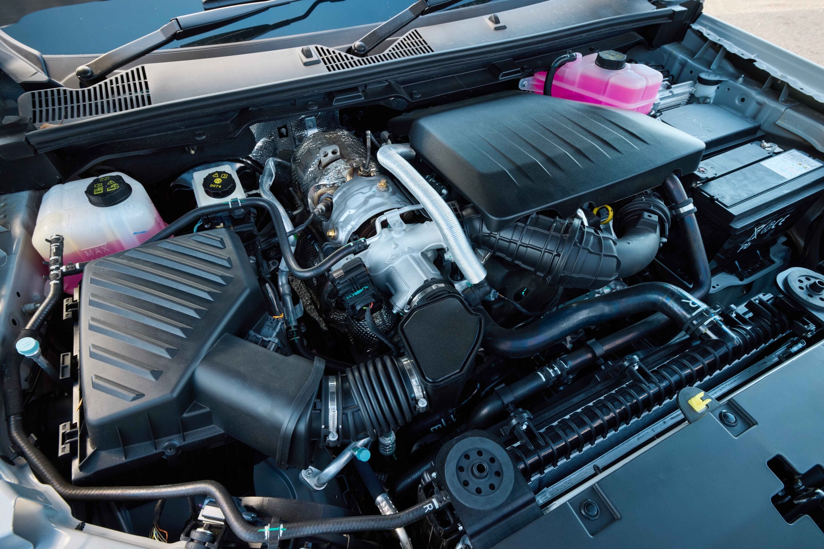 View of a car engine bay with pink coolant reservoir, hoses, and air intake in the foreground