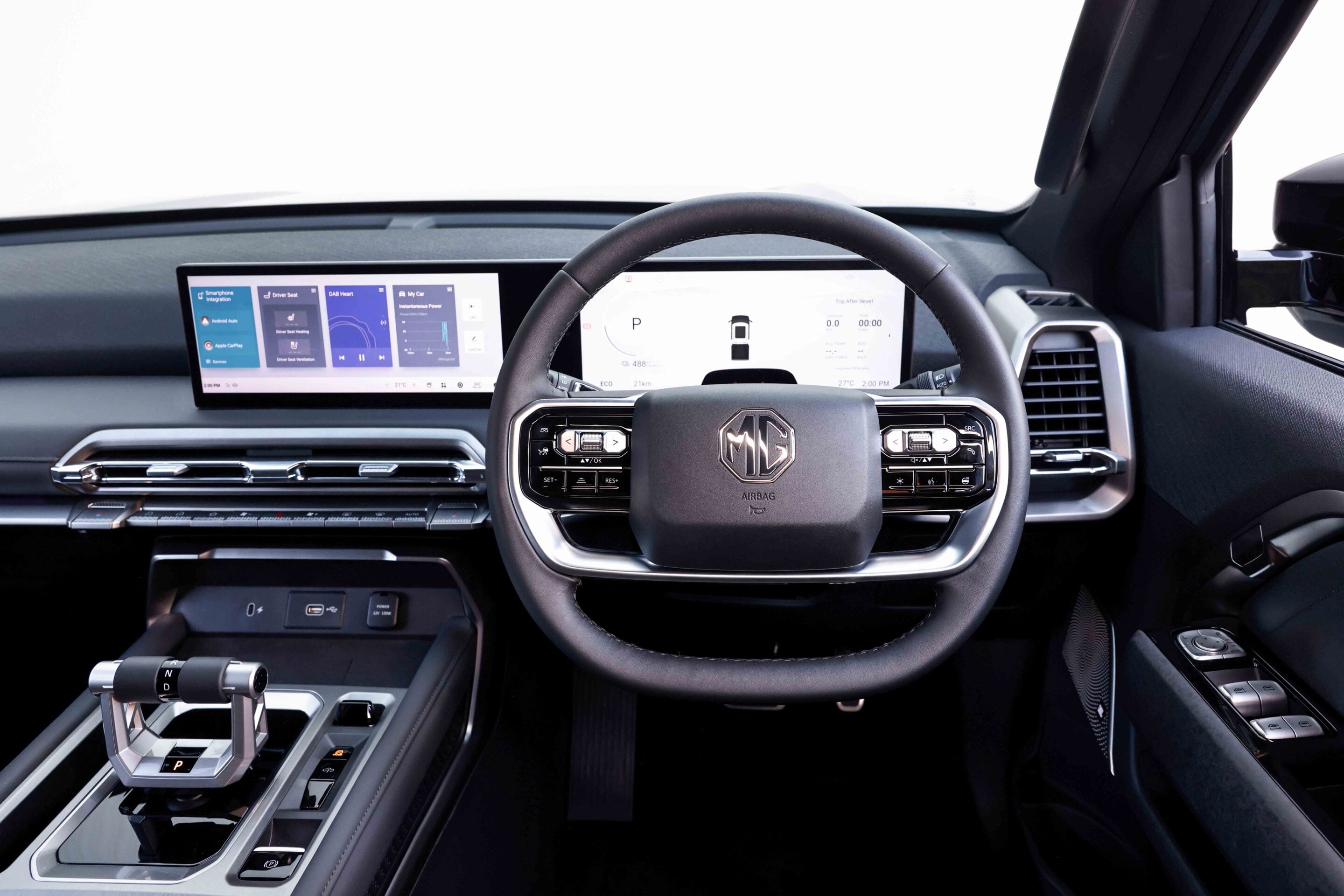 Modern car interior showing a wide dashboard touchscreen and digital instrument display behind the steering wheel and MG logo in the center.