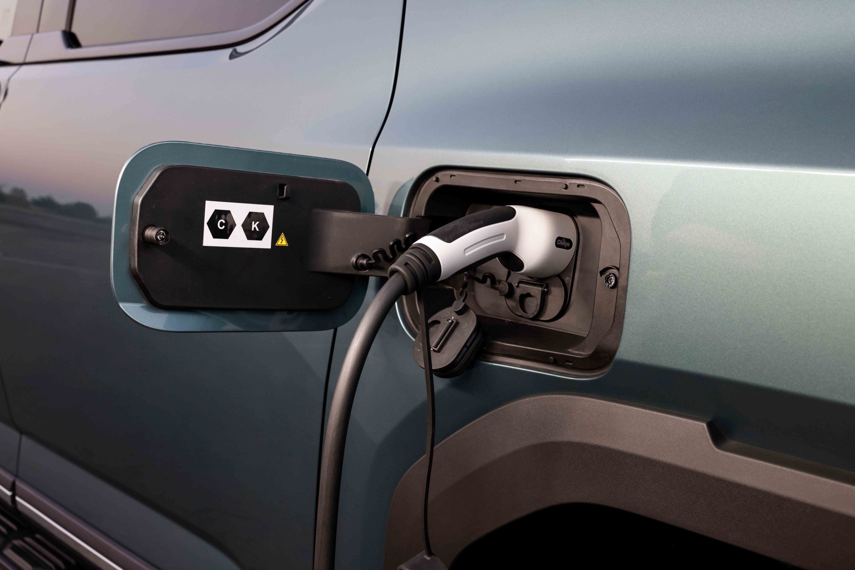 Electric car being charged; close-up of charging port with cable connected at dusk/new twilight lighting.