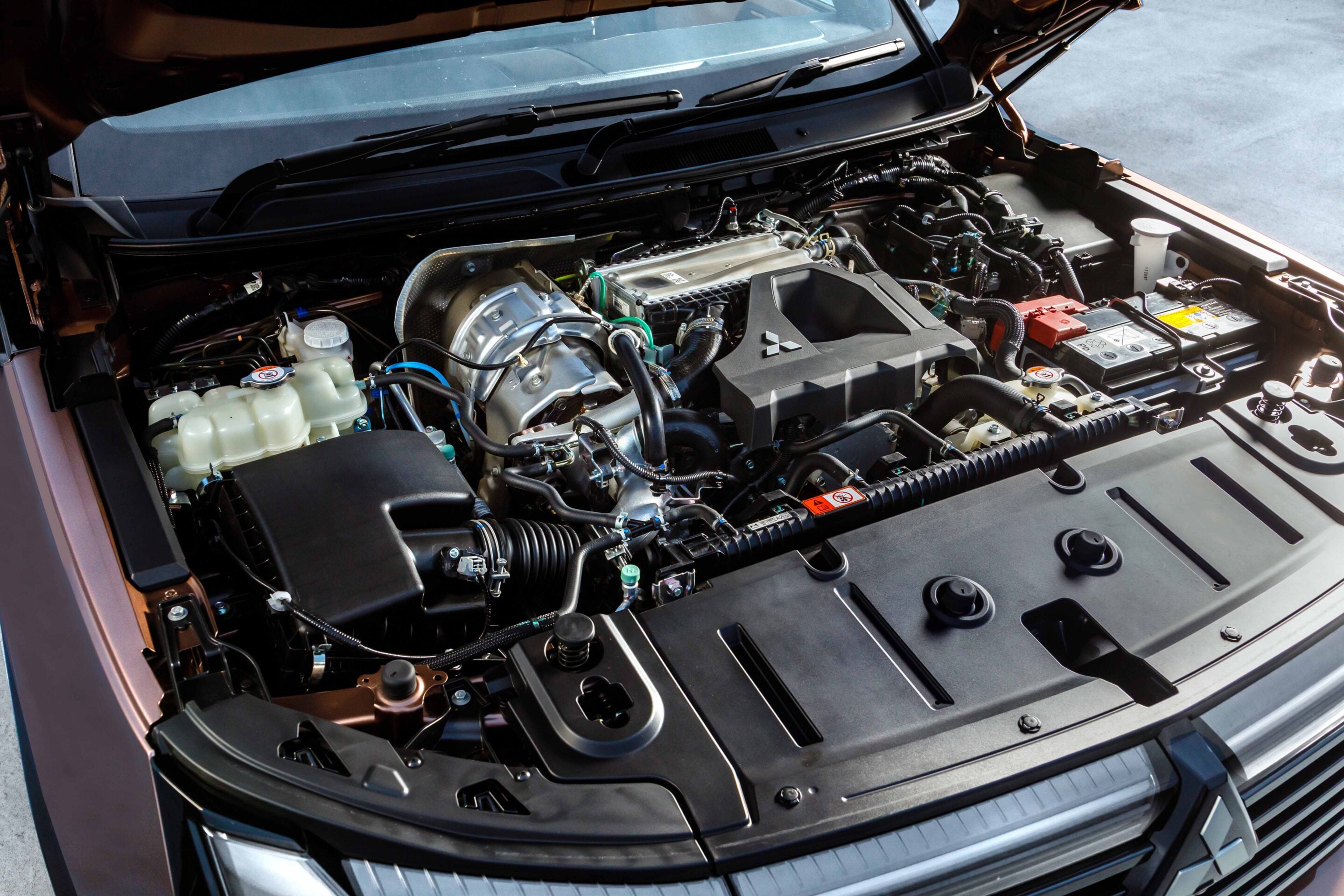 Open car hood showing engine bay with battery, coolant reservoir, and wiring. Her the components are neatly arranged under the hood of a modern vehicle.