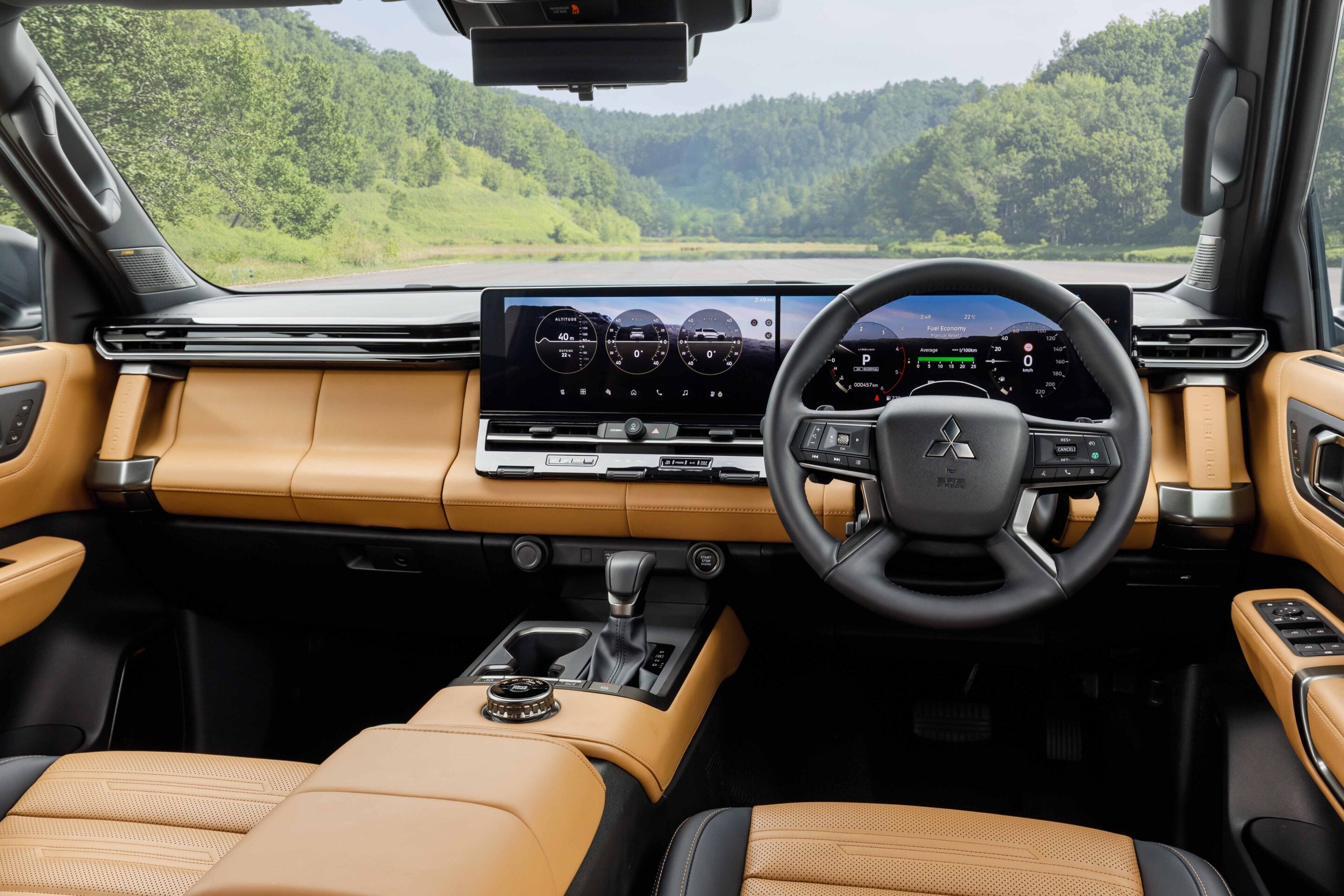 Interior view from the back seat of a luxury SUV, tan leather seats and a full digital instrument cluster with a steering wheel in front, greenery outside the windshield