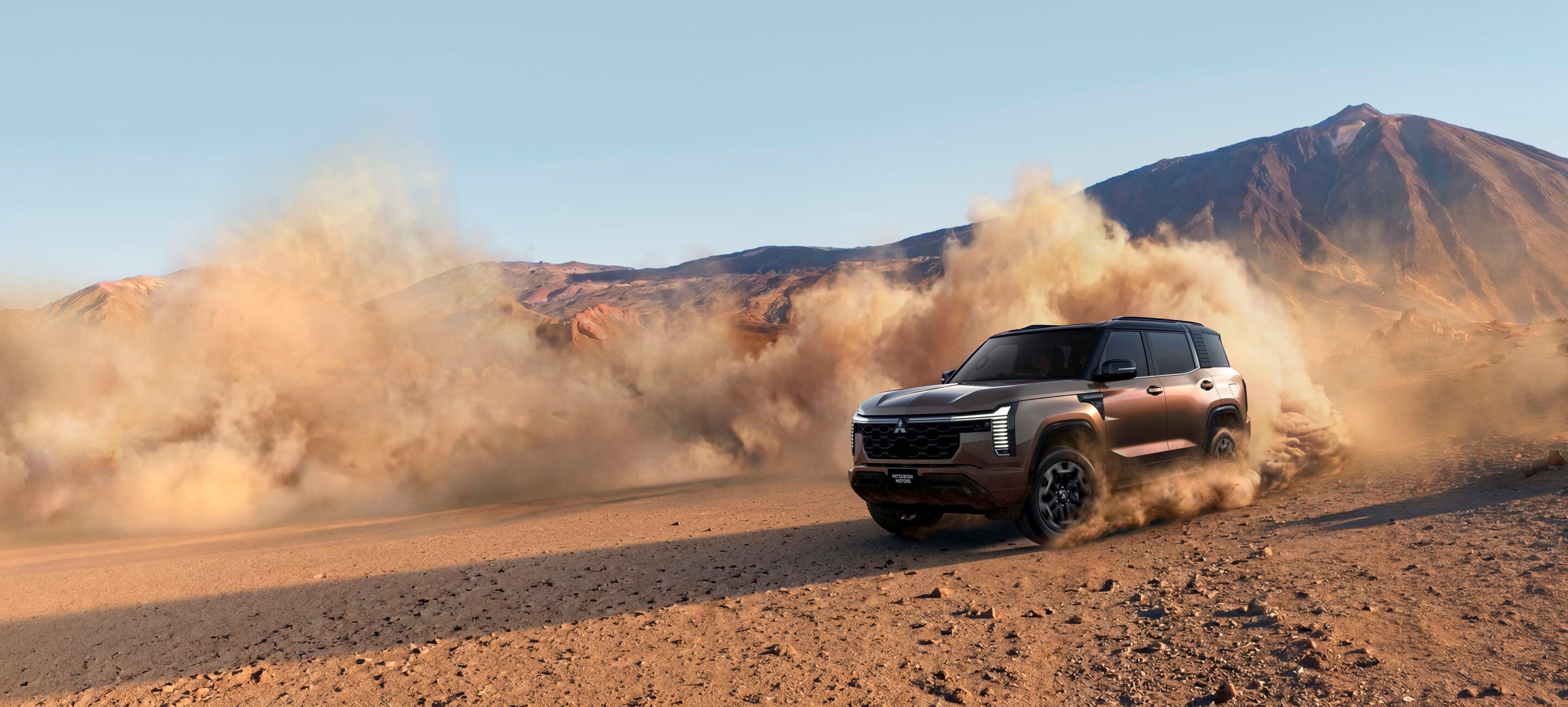 Bronze SUV kicking up dust while driving across a sandy desert with rocky mountains in the background primarily on the right side of the image.