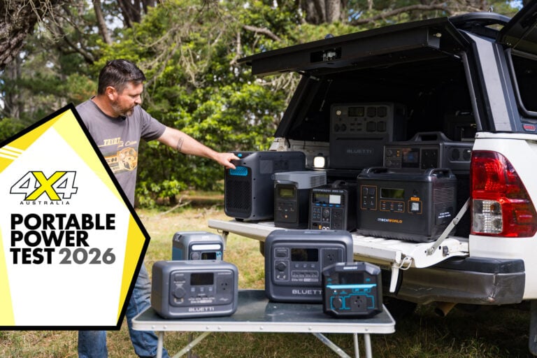 Man arranging portable power stations from the back of a SUV in an outdoor test setup, with a large 'Portable Power Test 2026' banner on the left.
