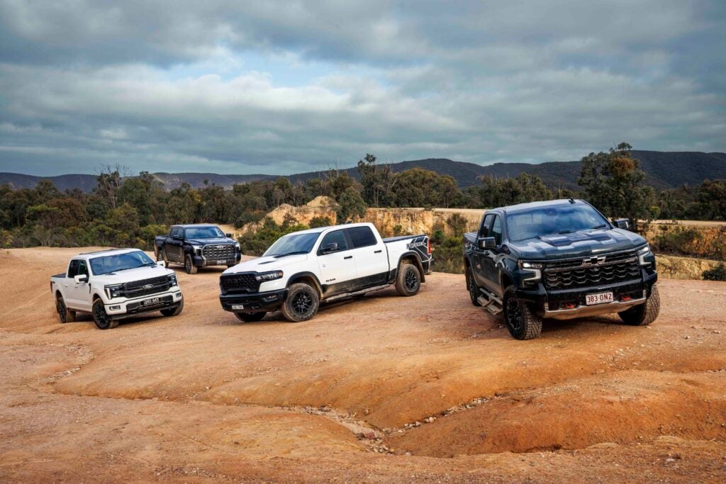 Group of pickup trucks parked on a dusty dirt lot with hills and cloudy sky in the background