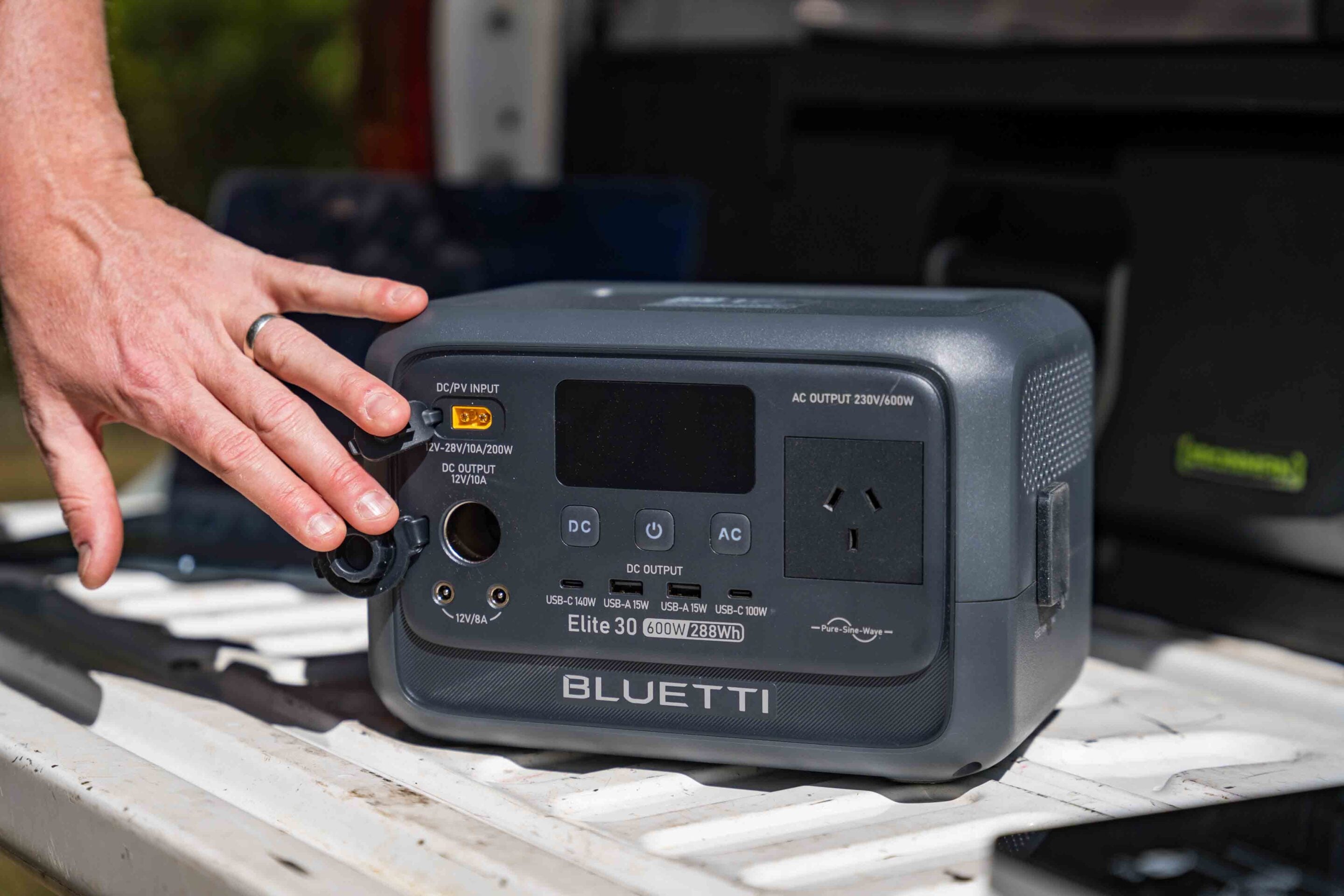 Close-up of a hand inserting a power connector into a Bluetti portable power station to charge it.