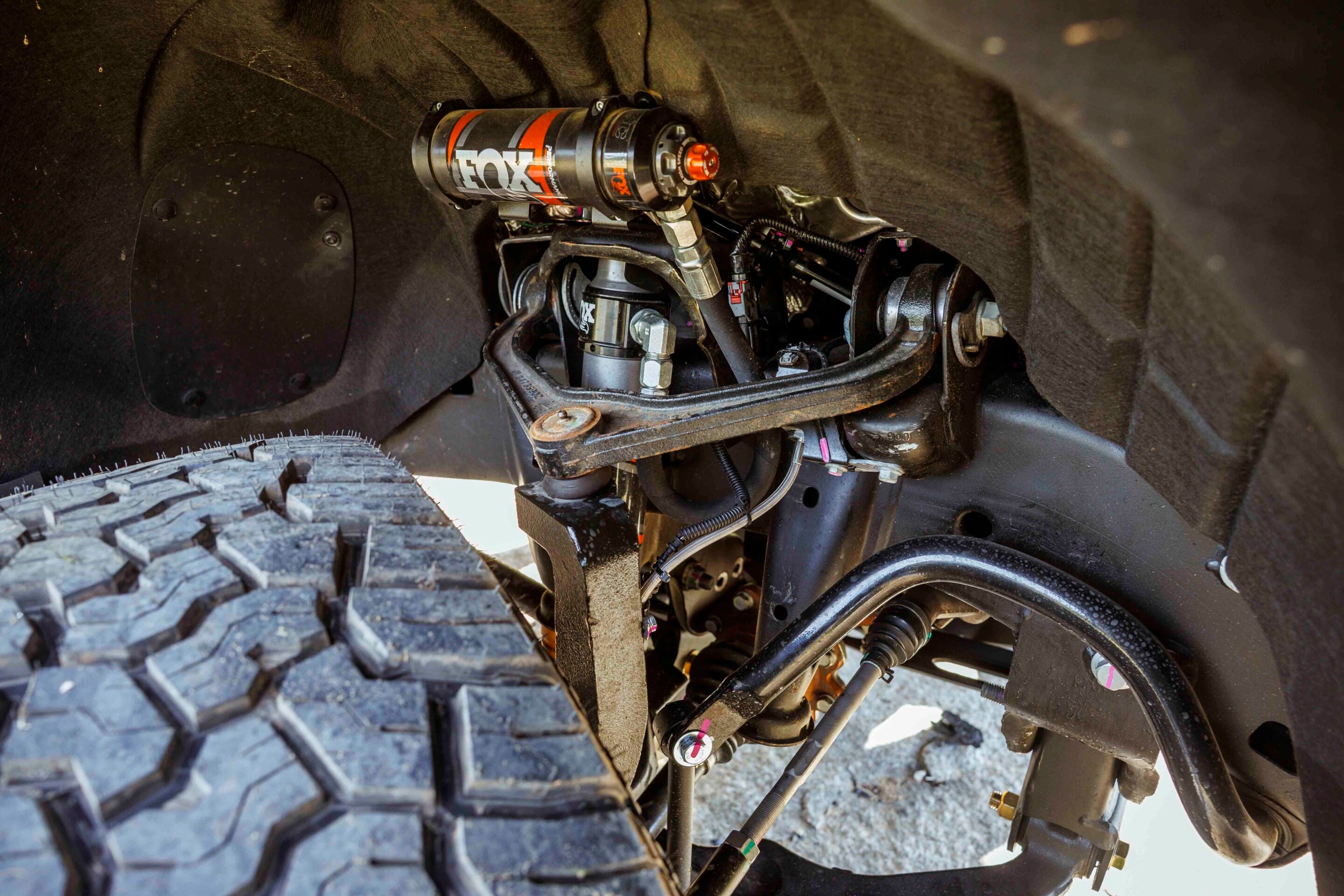 Close-up of an off-road vehicle's suspension, featuring a FOX shock absorber and rugged components inside the wheel well