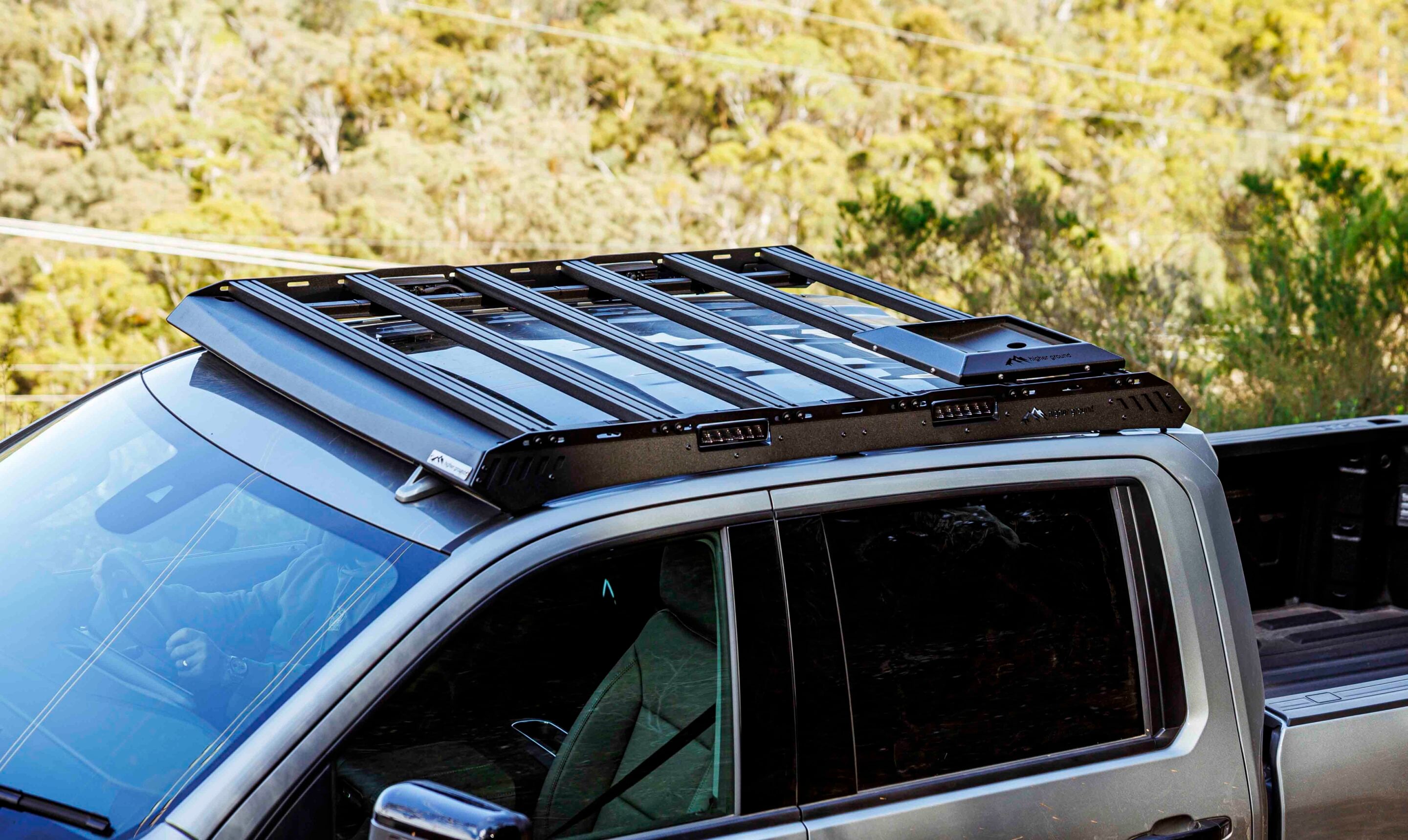 Black rooftop cargo rack mounted on a silver SUV, outdoors with green trees in the background (informative).