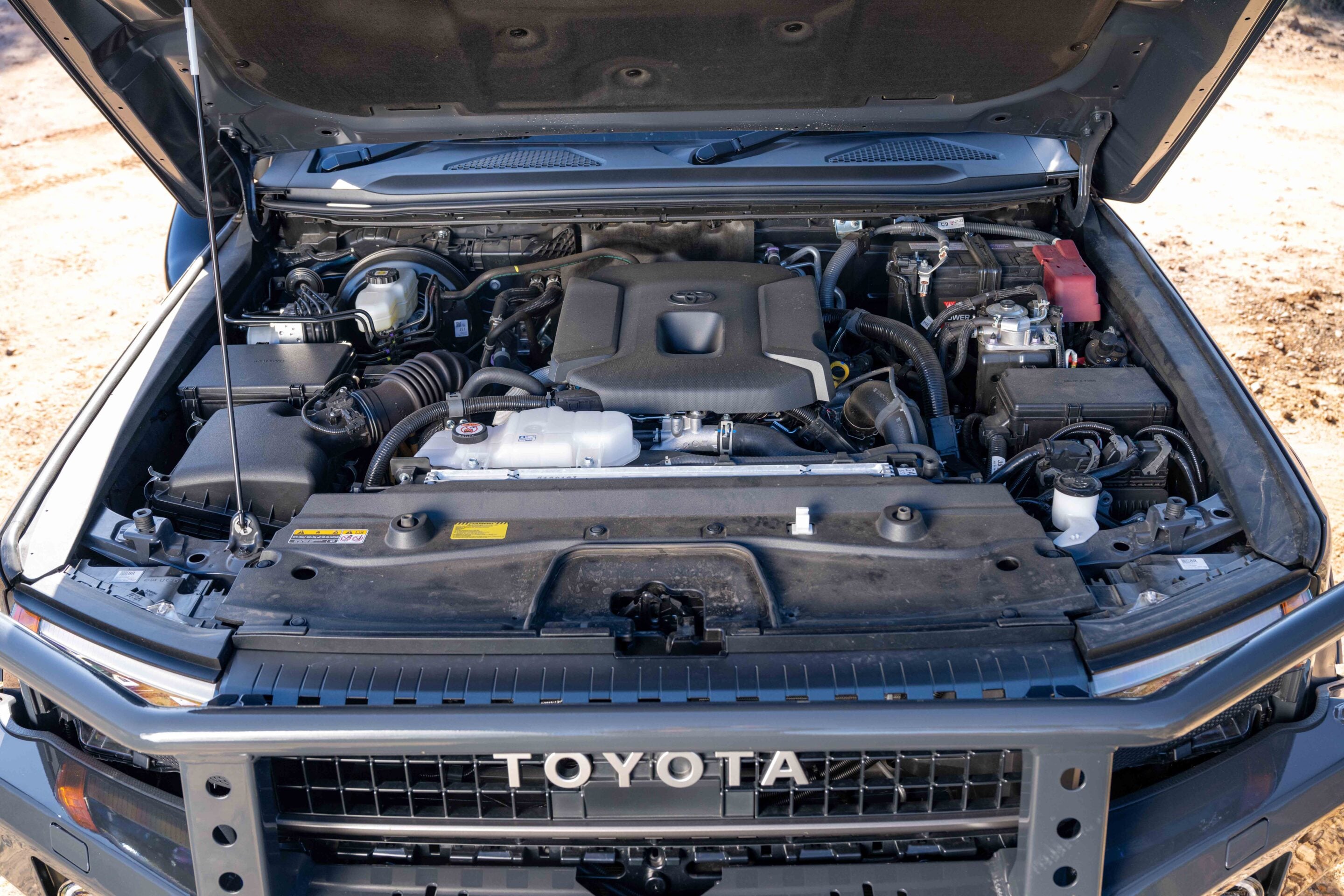 Open hood shows Toyota engine bay with a central plastic engine cover and visible battery on the right side.