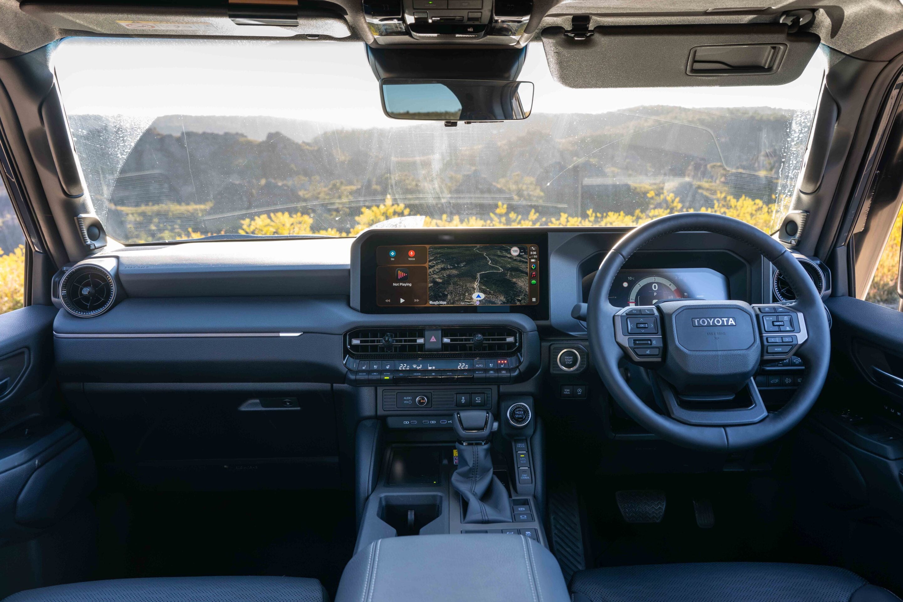Interior of a Toyota SUV showing a large center touchscreen with navigation, steering wheel, and climate controls visible.