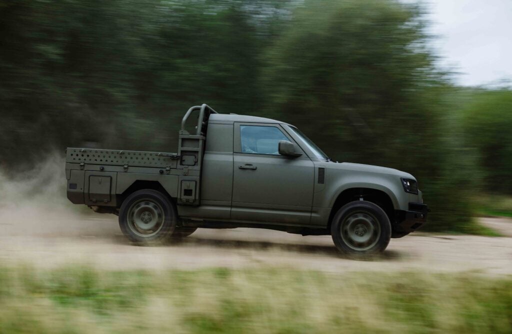 Green military-style pickup speeding along a dusty off-road trail with blurred trees in the background