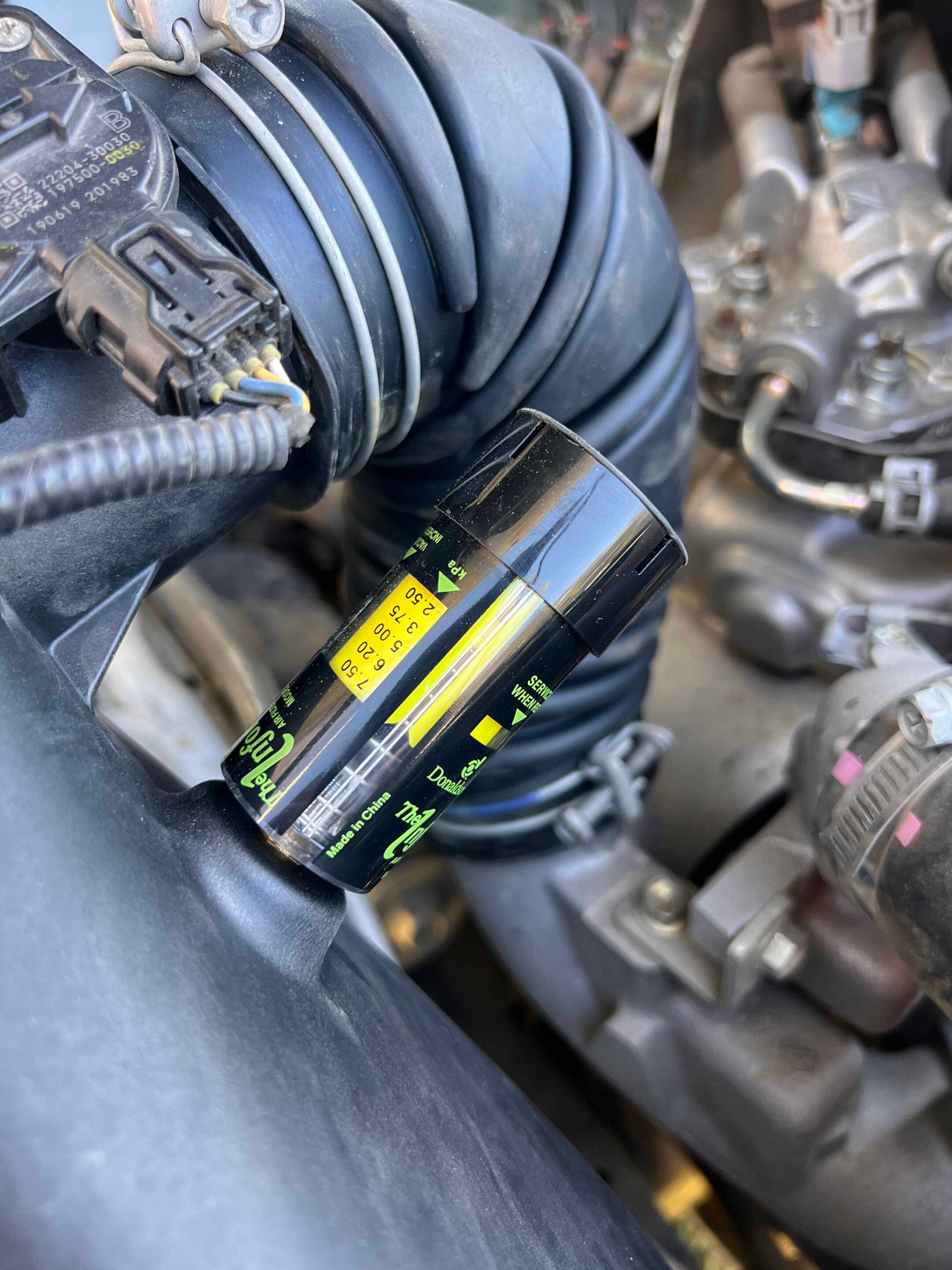 Close-up of a black inspection flashlight clipped beside engine hoses under the car hood.