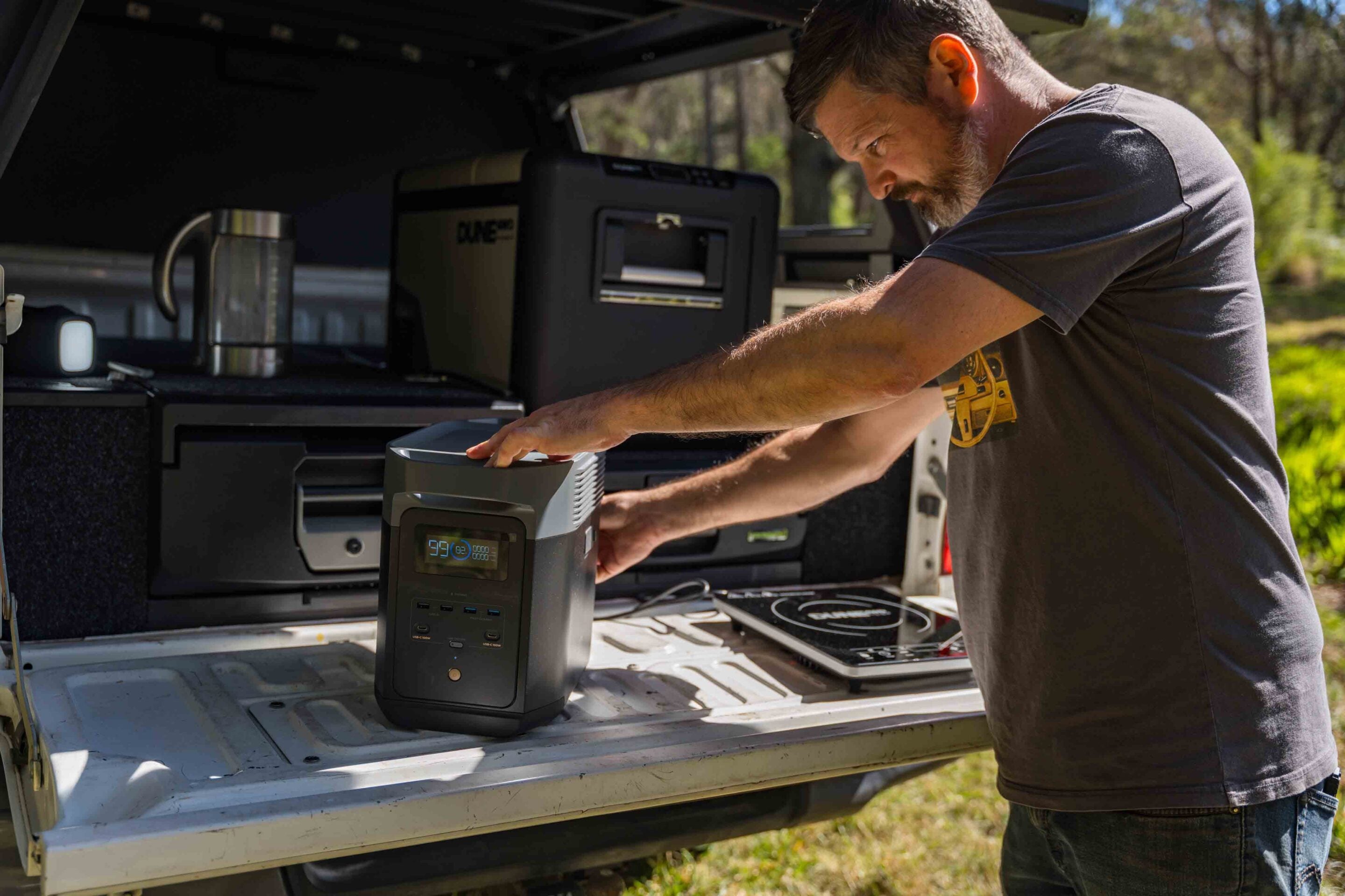Man standing at an open truck bed, operating a portable power station with a digital display.