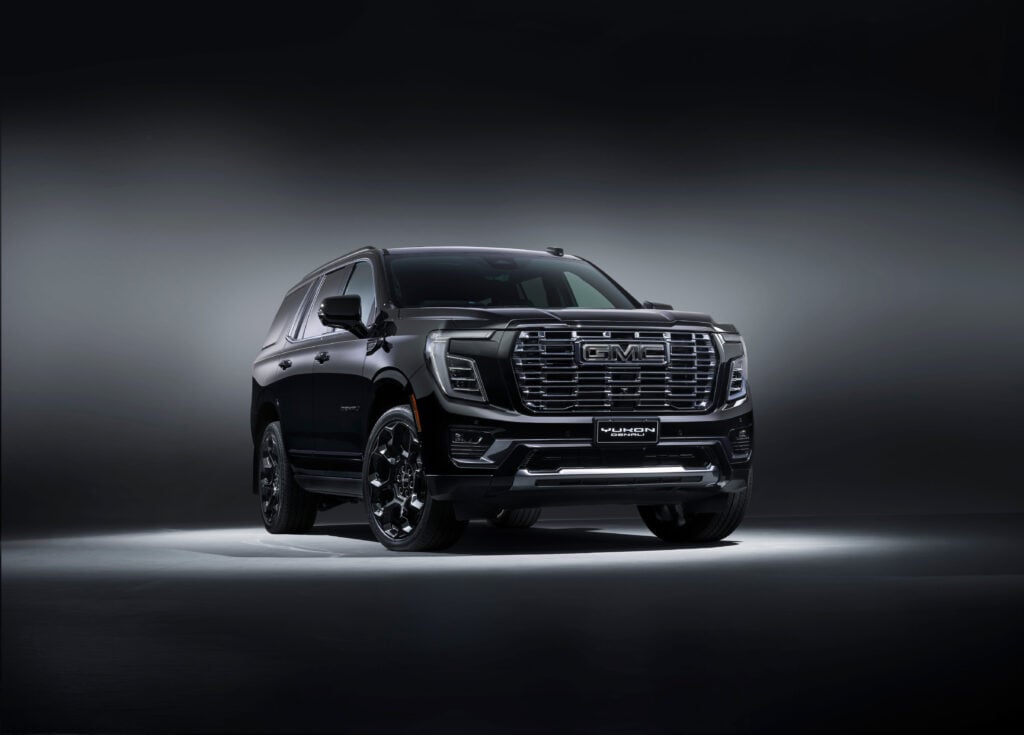 Front three-quarter view of a dark gray GMC Yukon Denali SUV in a studio setting with a gradient background.