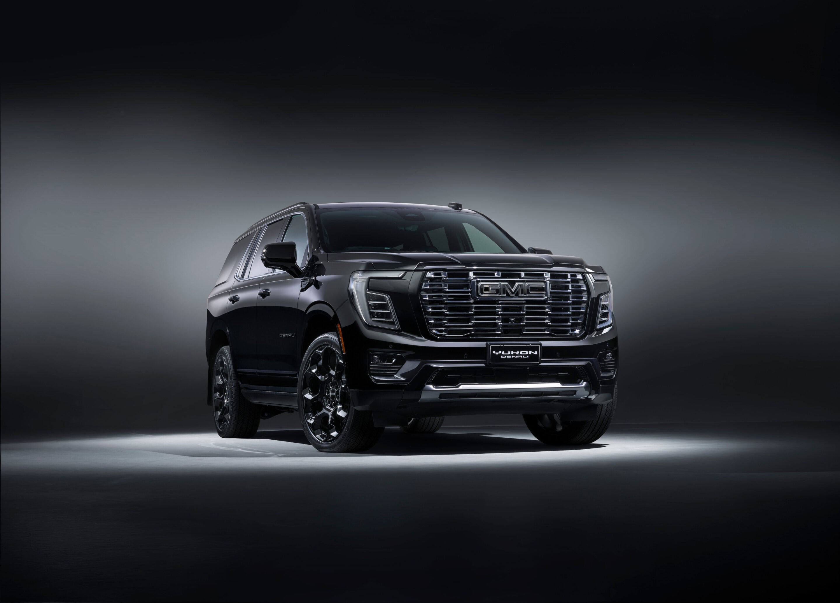 Front three-quarter view of a dark gray GMC Yukon Denali SUV in a studio setting with a gradient background.