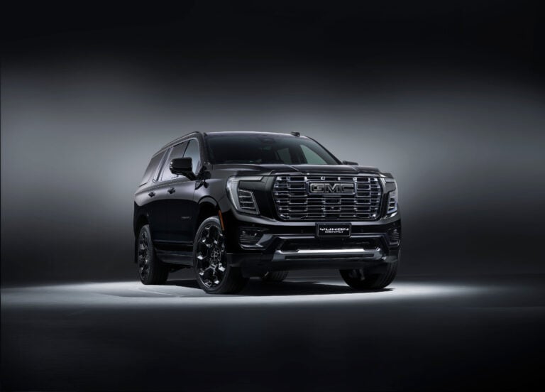 Front three-quarter view of a dark gray GMC Yukon Denali SUV in a studio setting with a gradient background.