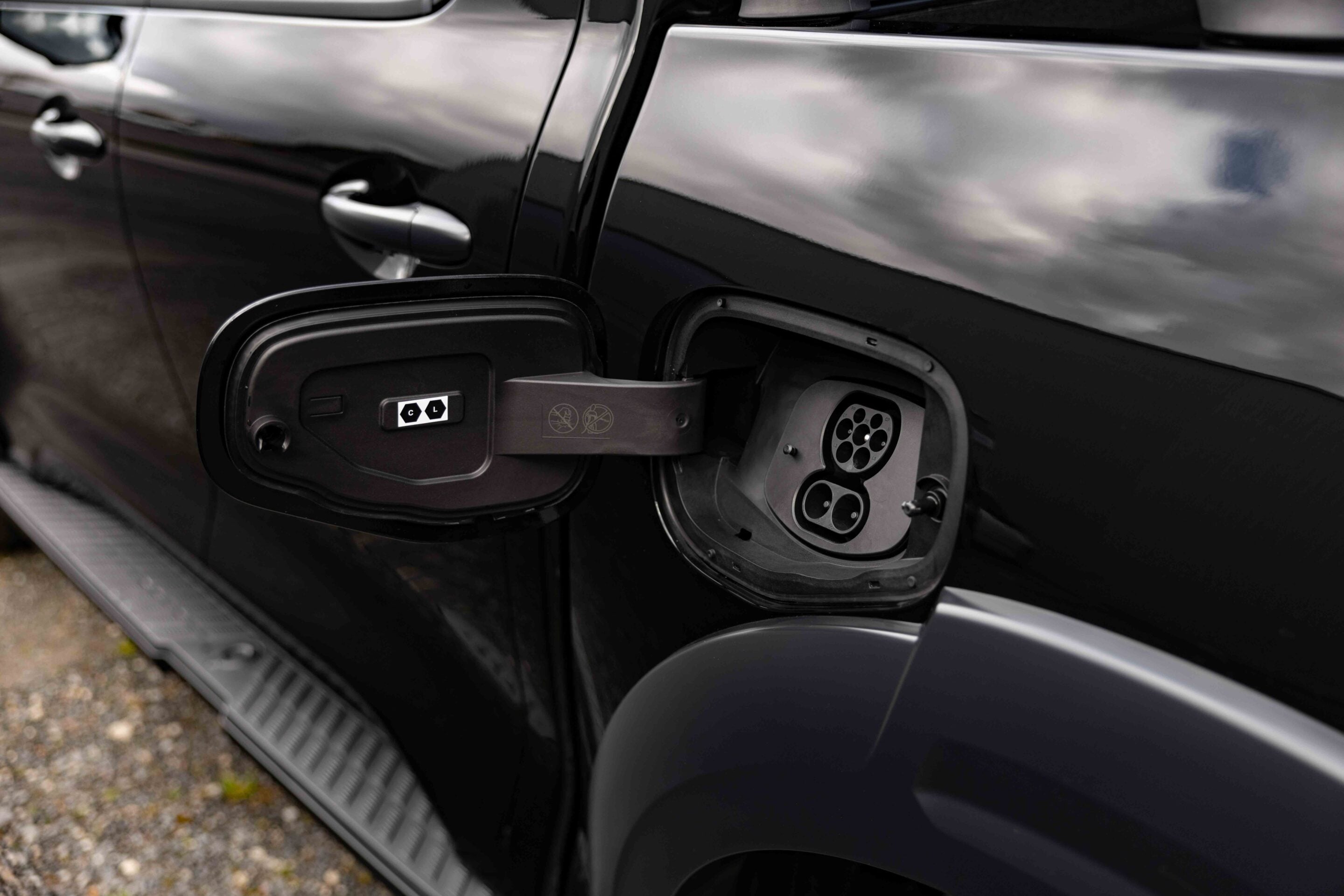 Open charging port on a black SUV, showing a circular multi-pin connector inside the receptacle.