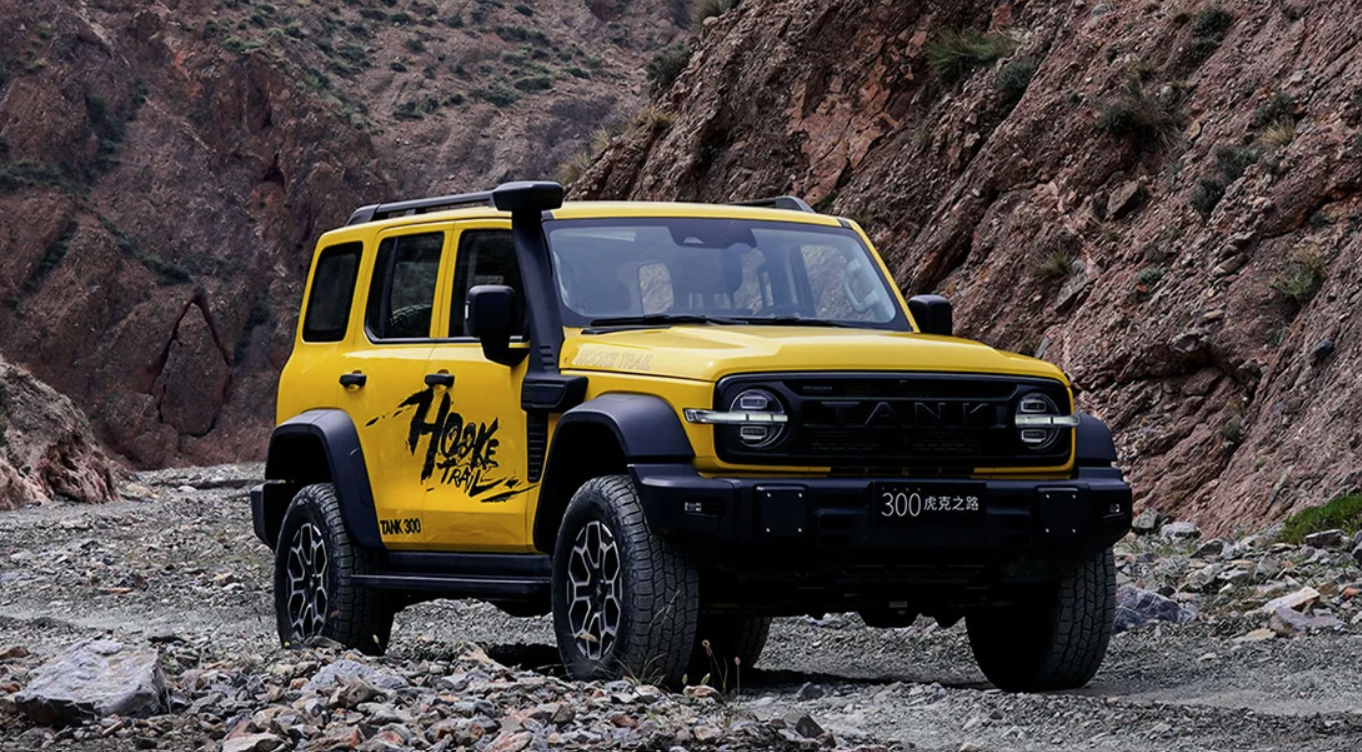Yellow off-road SUV (Tank 300) seen from the front-left, parked on a rocky mountain pass with red cliffs in the background.