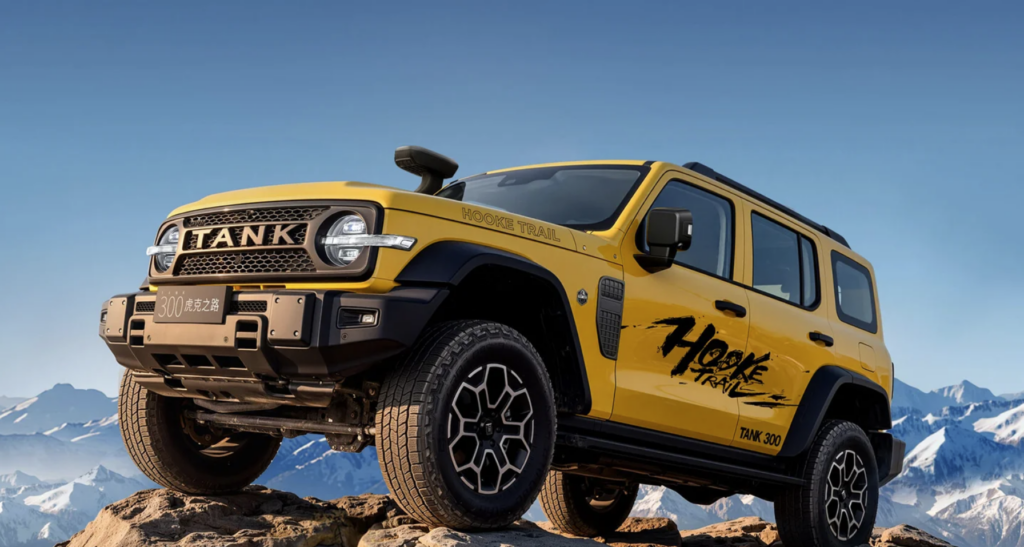 Yellow off-road Tank 300 SUV climbing a rocky slope with snow-capped mountains in the background.