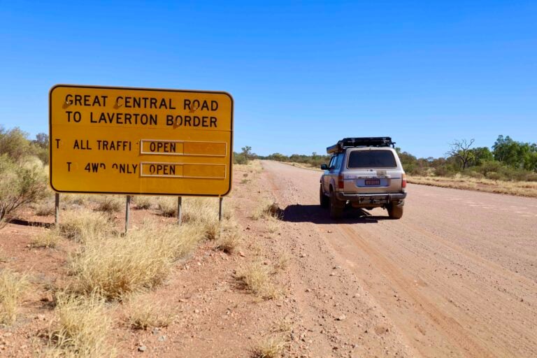 Yellow road sign on a dusty rural road, directing to Laverton border and Great Central Road; SUV parked on the right.