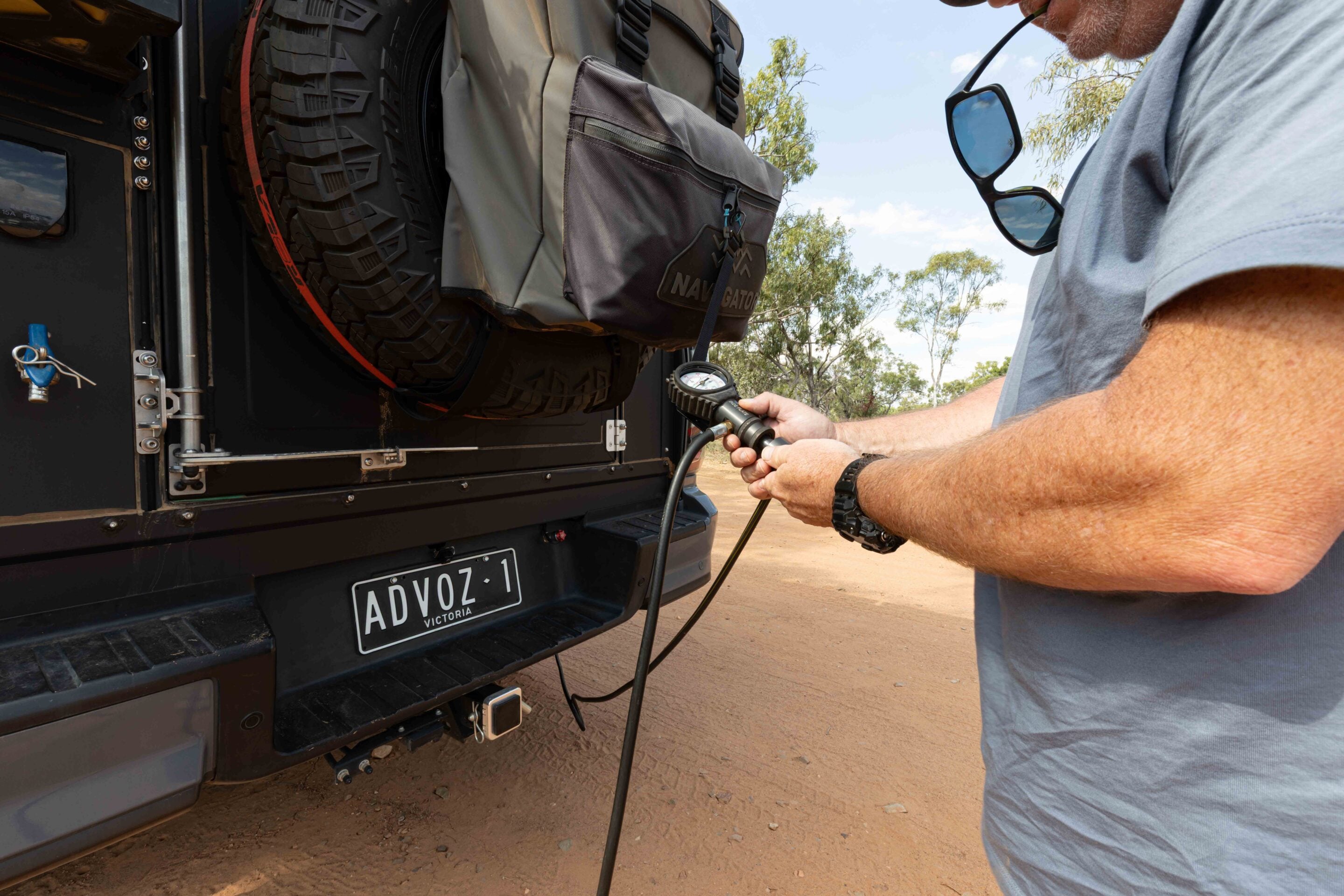 Man inflating a mounted spare tire on the back of a black SUV using an air hose and gauge.