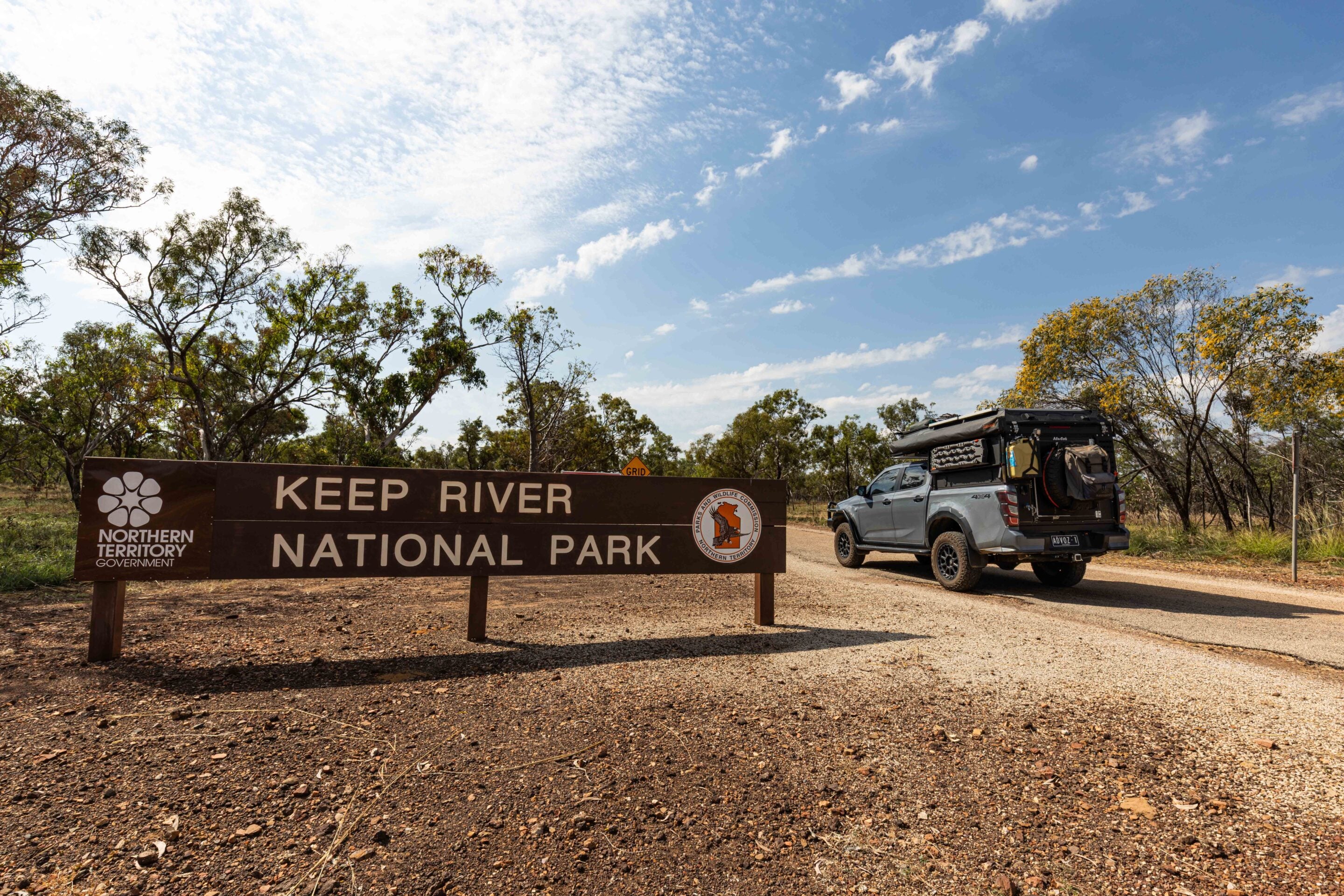 Keep River National Park sign with Northern Territory Government logo; a camper van parked to the right, trees and blue sky above.