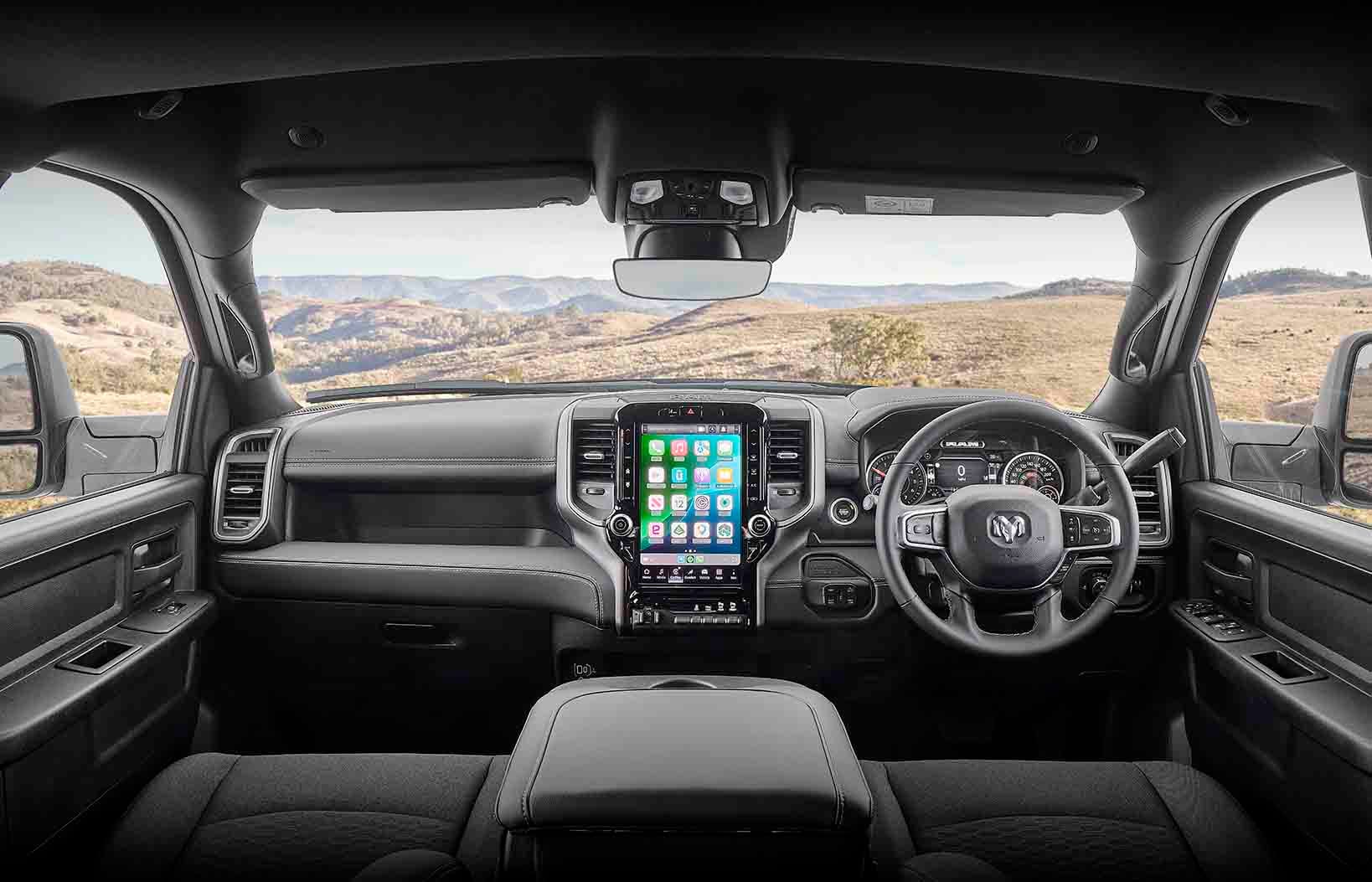 Right-hand-drive pickup interior with a tall vertical touchscreen infotainment system between the central vents and a desert landscape visible through the windshield