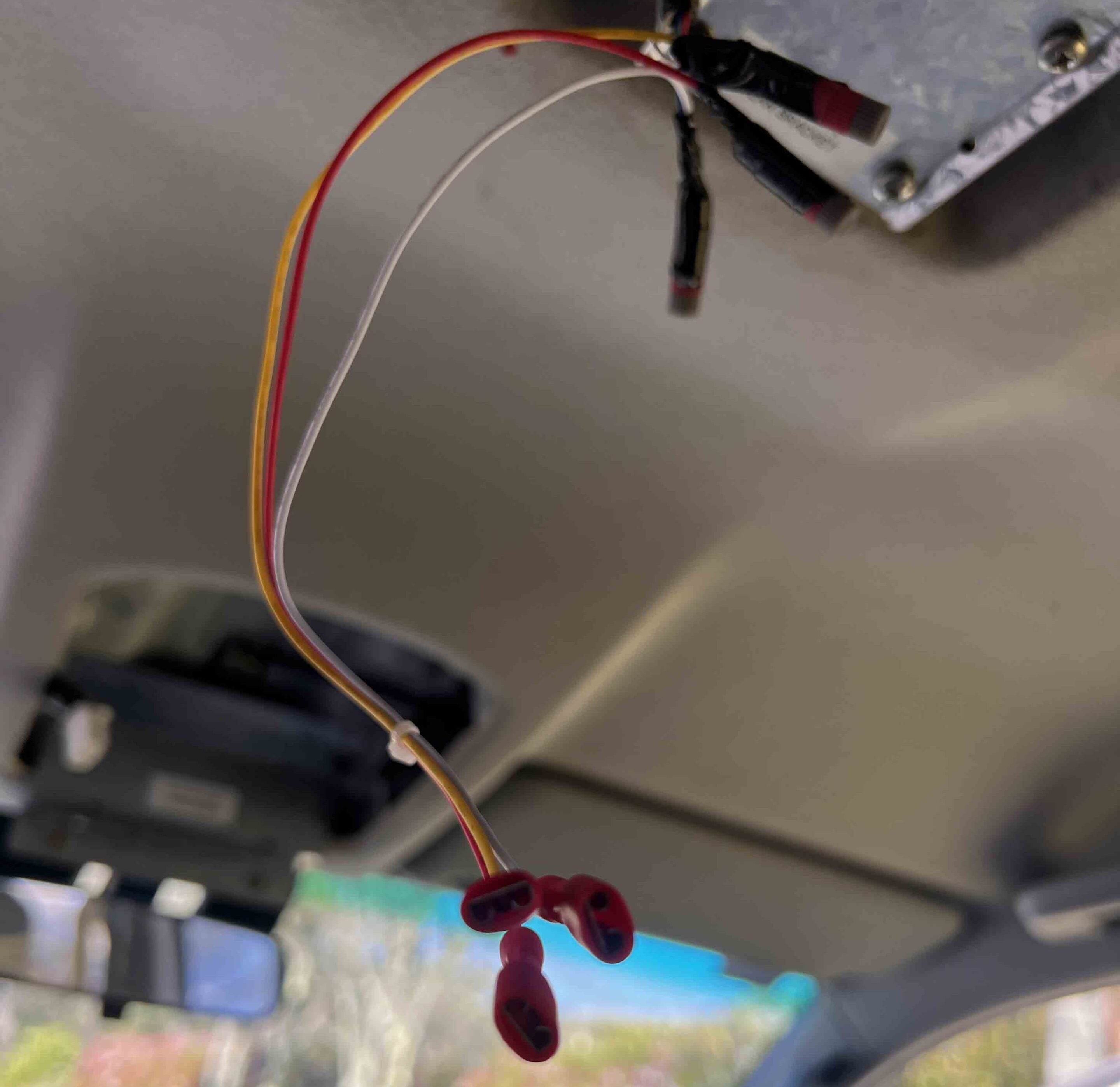 Close-up of red, yellow, and white wires with a red connector hanging inside a metallic enclosure, likely part of an electrical device.