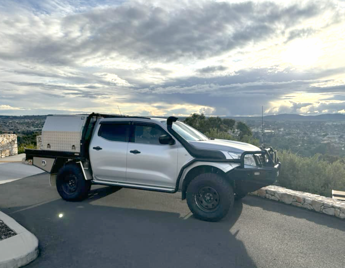 Silver four-door pickup truck with a utility toolbox parked on a scenic overlook, view of a valley beneath cloudy sky, stone barrier on the right chevron wall left.