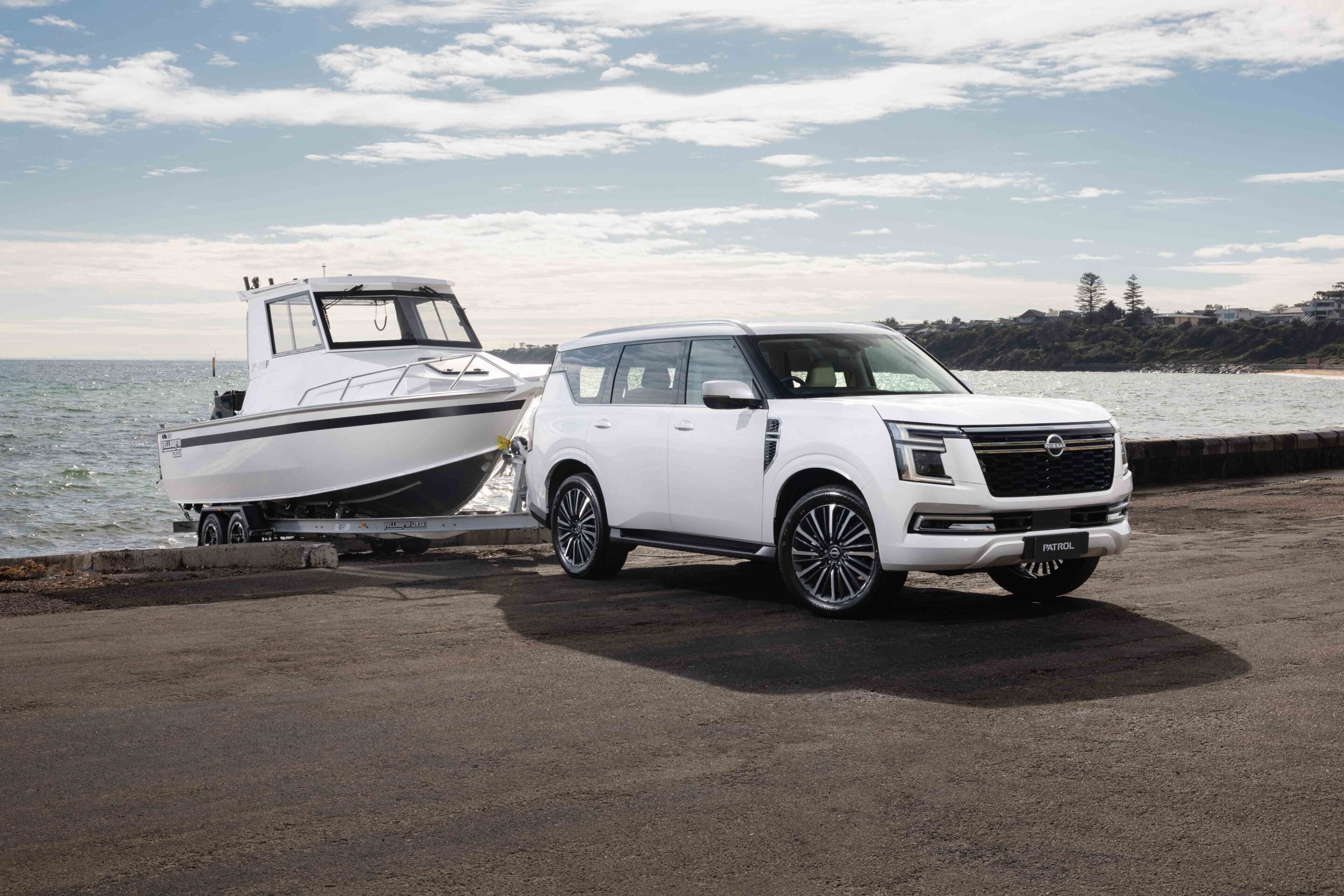 White Nissan Patrol SUV on a trailer beside a white motorboat at the harbor.