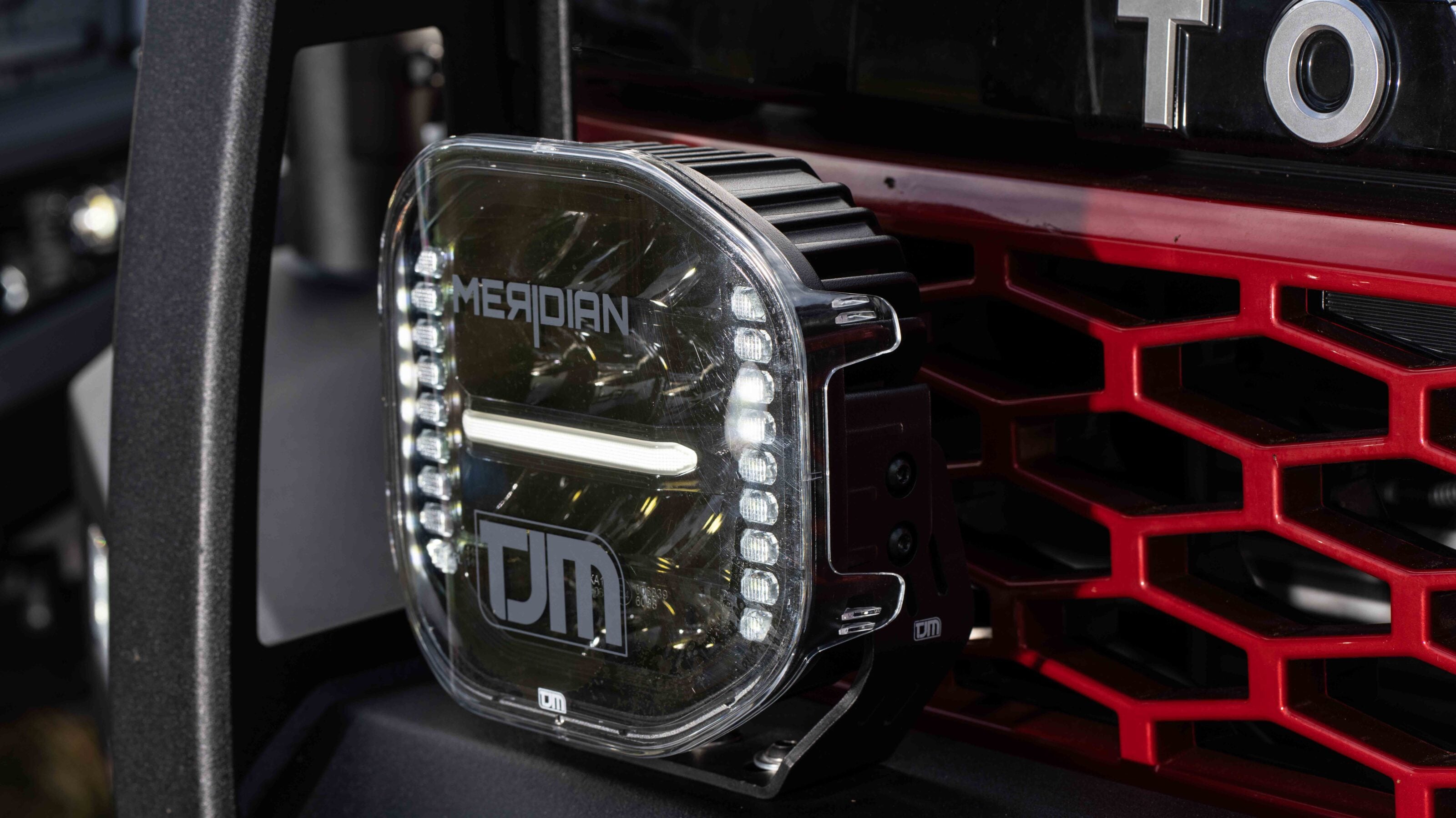 Close-up of a rectangular off-road headlight with LED accents beside a red grille.