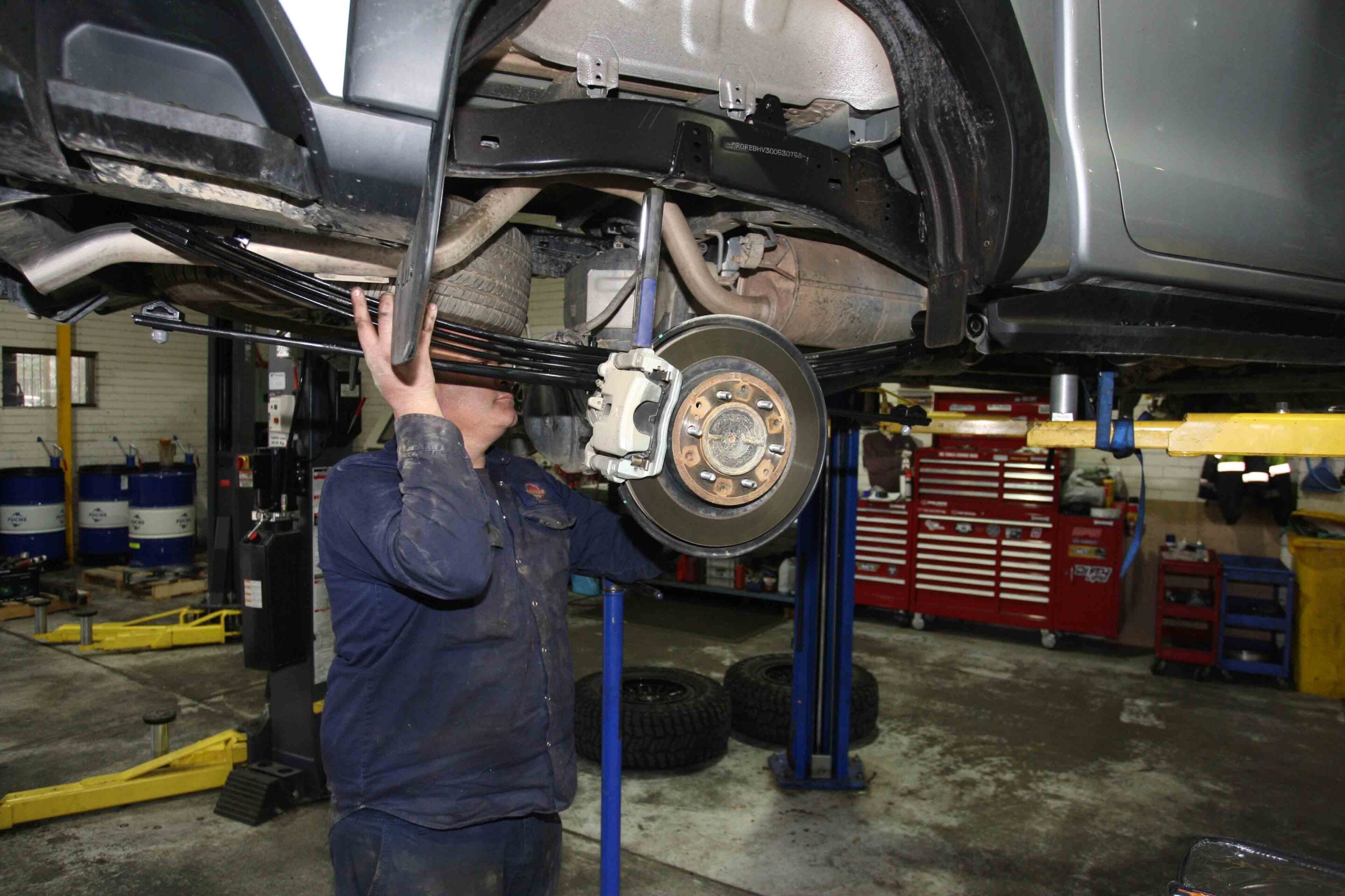 Mechanic inspecting the rear of a raised vehicle, brake rotor and suspension visible under the car in an auto shop