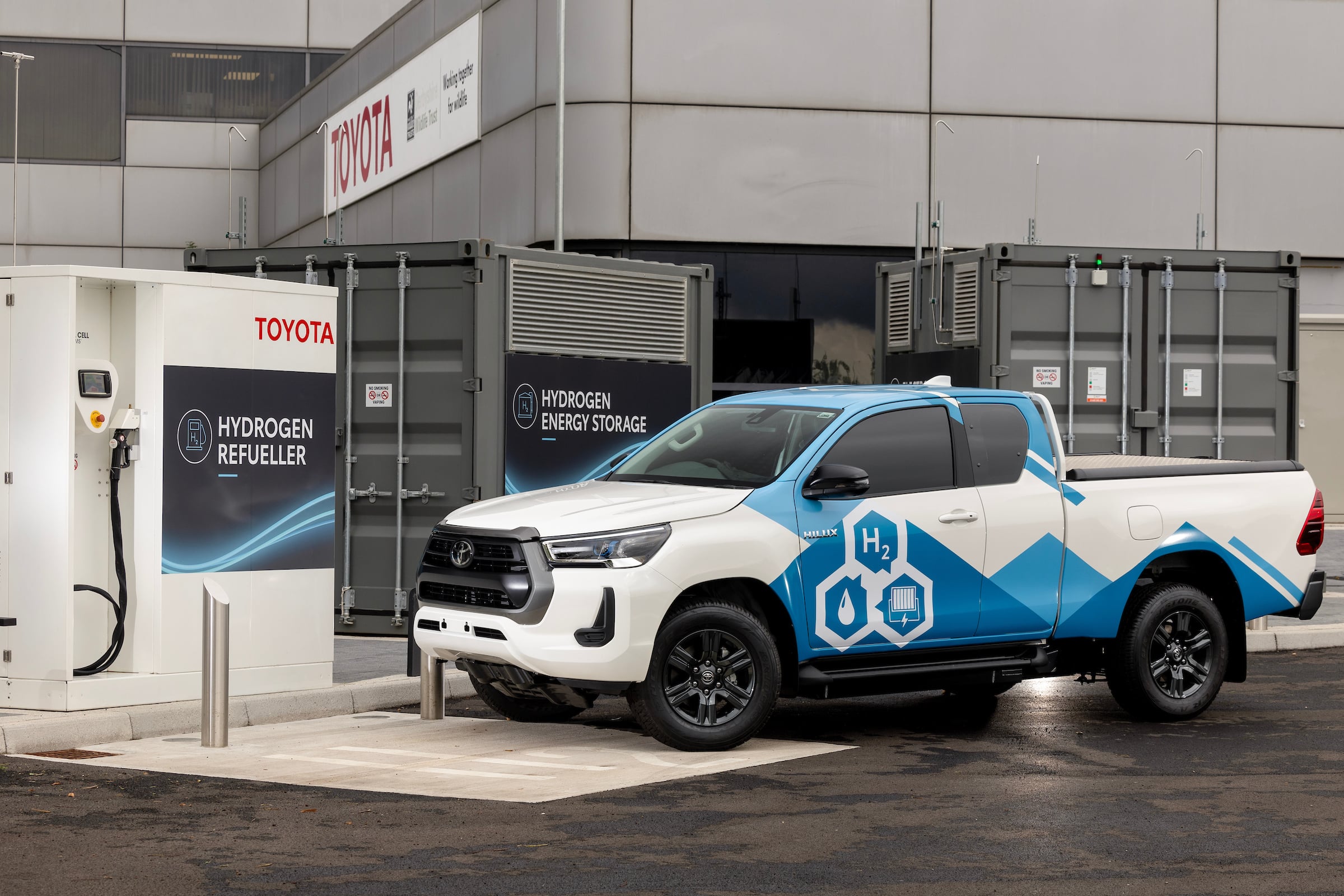 Hydrogen energy storage units at a fueling site with a Toyota sign and a blue-and-white hydrogen truck parked in front.