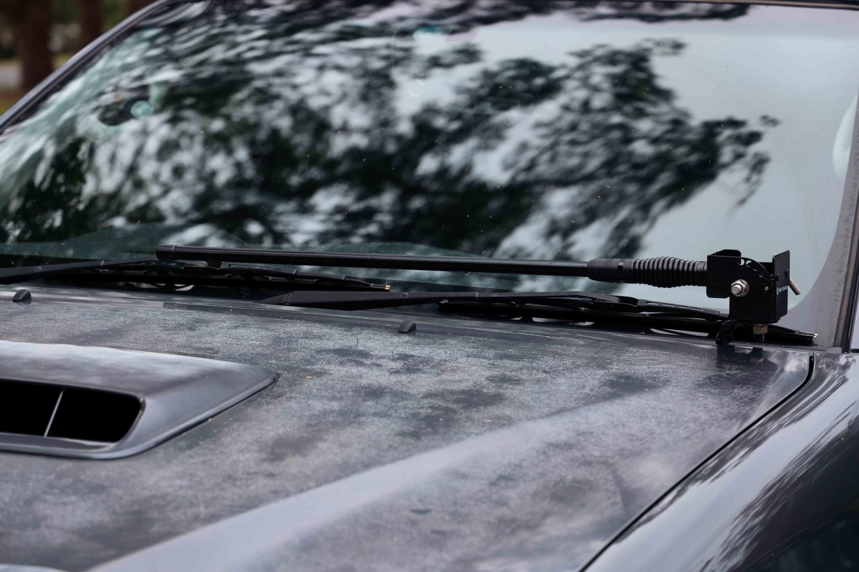 Close-up of a car windshield with a wiper blade resting on the hood and a mounted device on the right side of the glass.