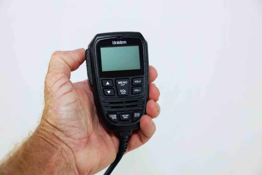 Hand holding a black Uniden handheld scanner with a small display and keypad visible.