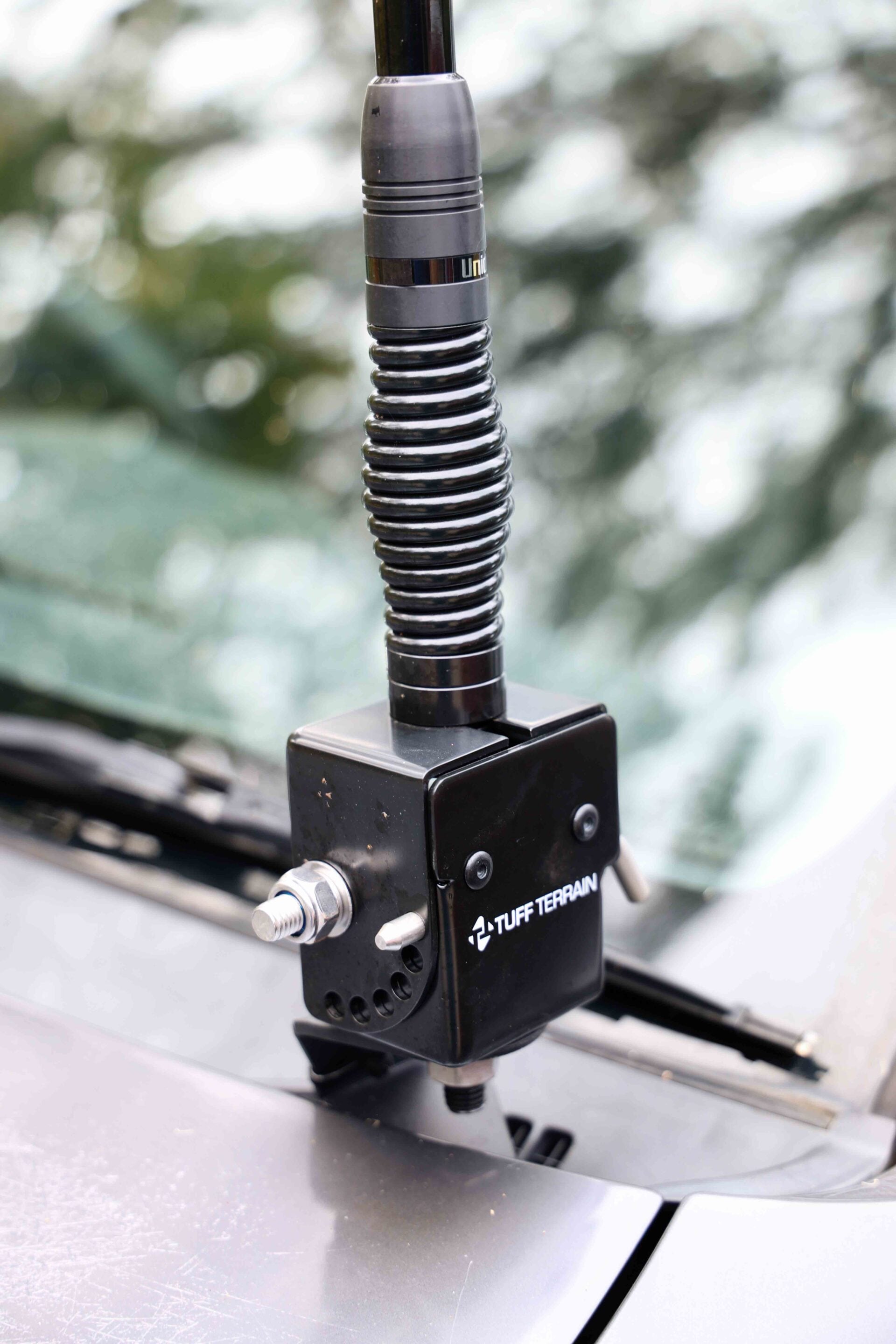 Close-up of a black coil spring shock absorber mounted on a vehicle, with a square base labeled 'TUFF TERRAIN' and a bolt at the front.