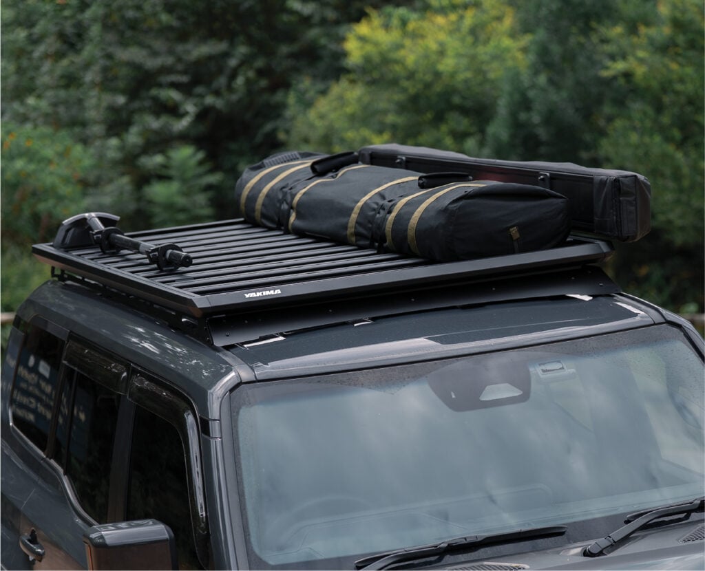 SUV with a roof rack holding two black duffel bags and a long rectangular bag, secured for travel