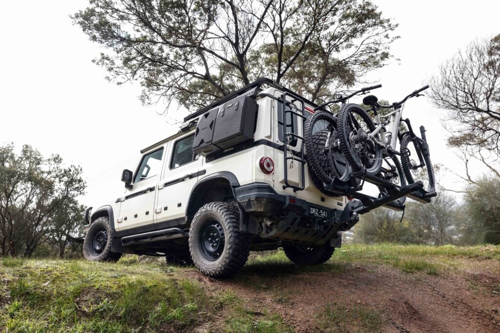 White off-road SUV with a bike rack carrying two mountain bikes on a grassy trail outside.