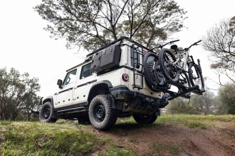 White off-road SUV with a bike rack carrying two mountain bikes on a grassy trail outside.