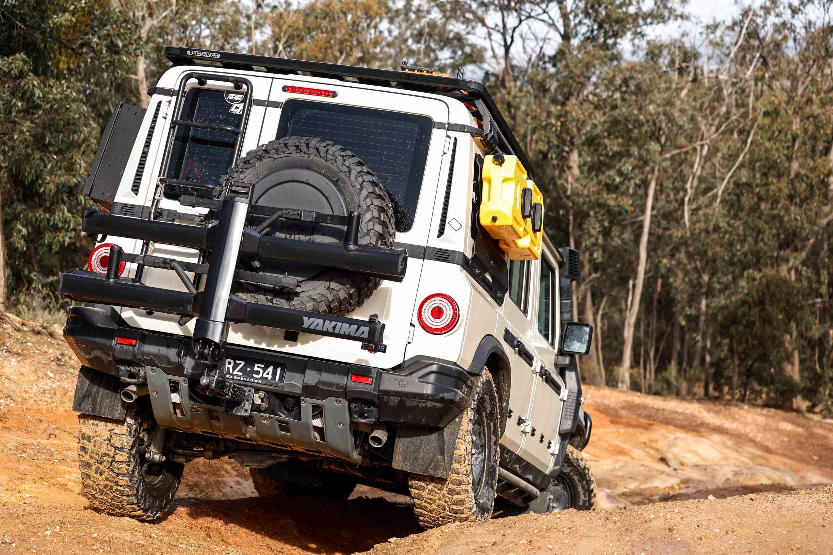 Off-road SUV tilted on a dirt track with a mounted spare tire and a yellow jerry can on the side, rugged outdoor scene
