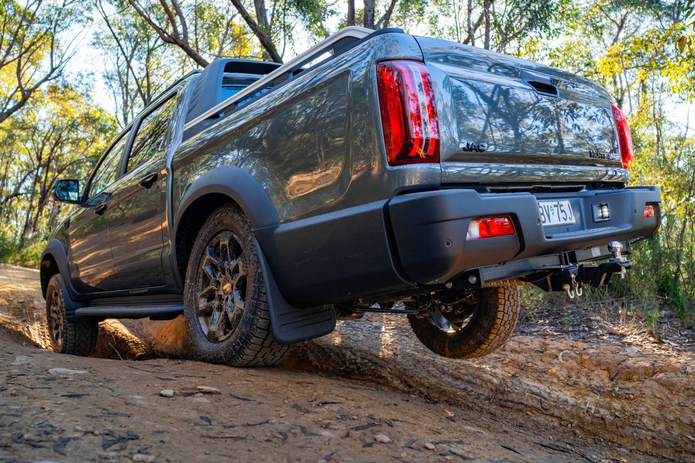 Rear three-quarter view of a gray pickup truck parked on a dirt trail among trees in a forest.