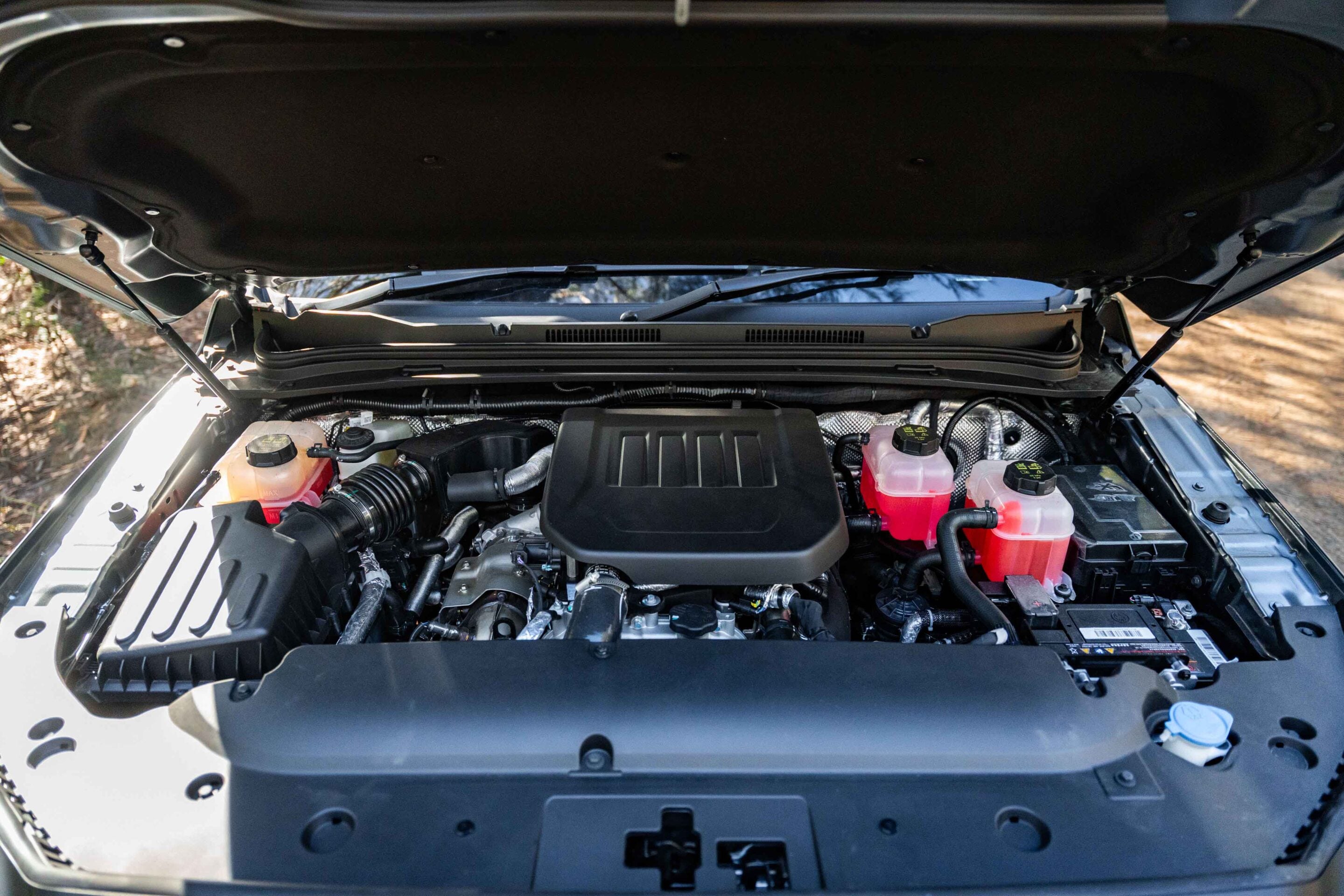 Under-hood view of a car with the hood raised, showing the engine, battery, and coolant reservoirs visible at the front corners.