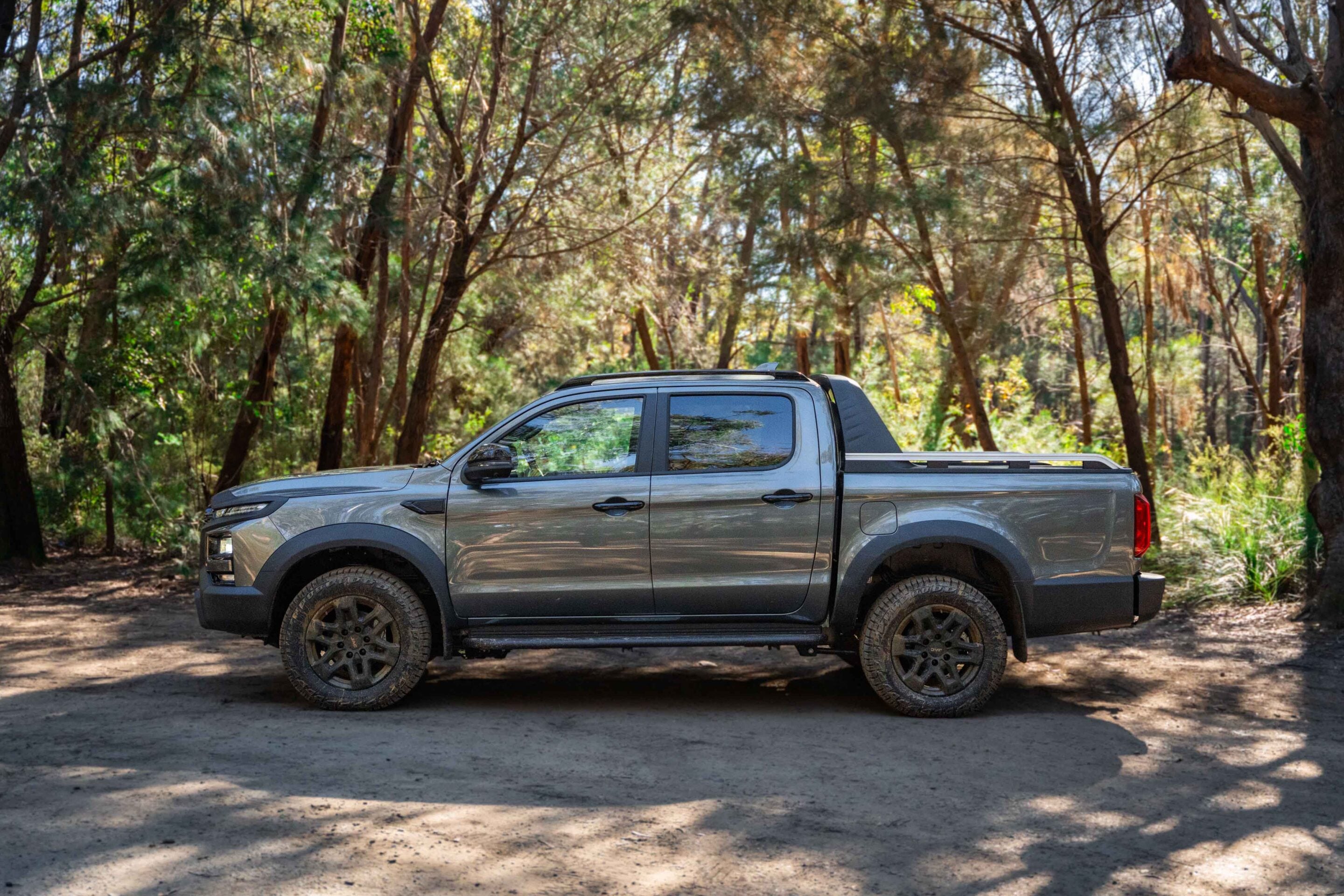 Gray pickup truck parked on a dirt road surrounded by dense trees in a forest setting.