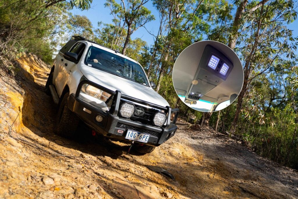 White off-road SUV navigating a rocky dirt trail through a forest under a clear blue sky.