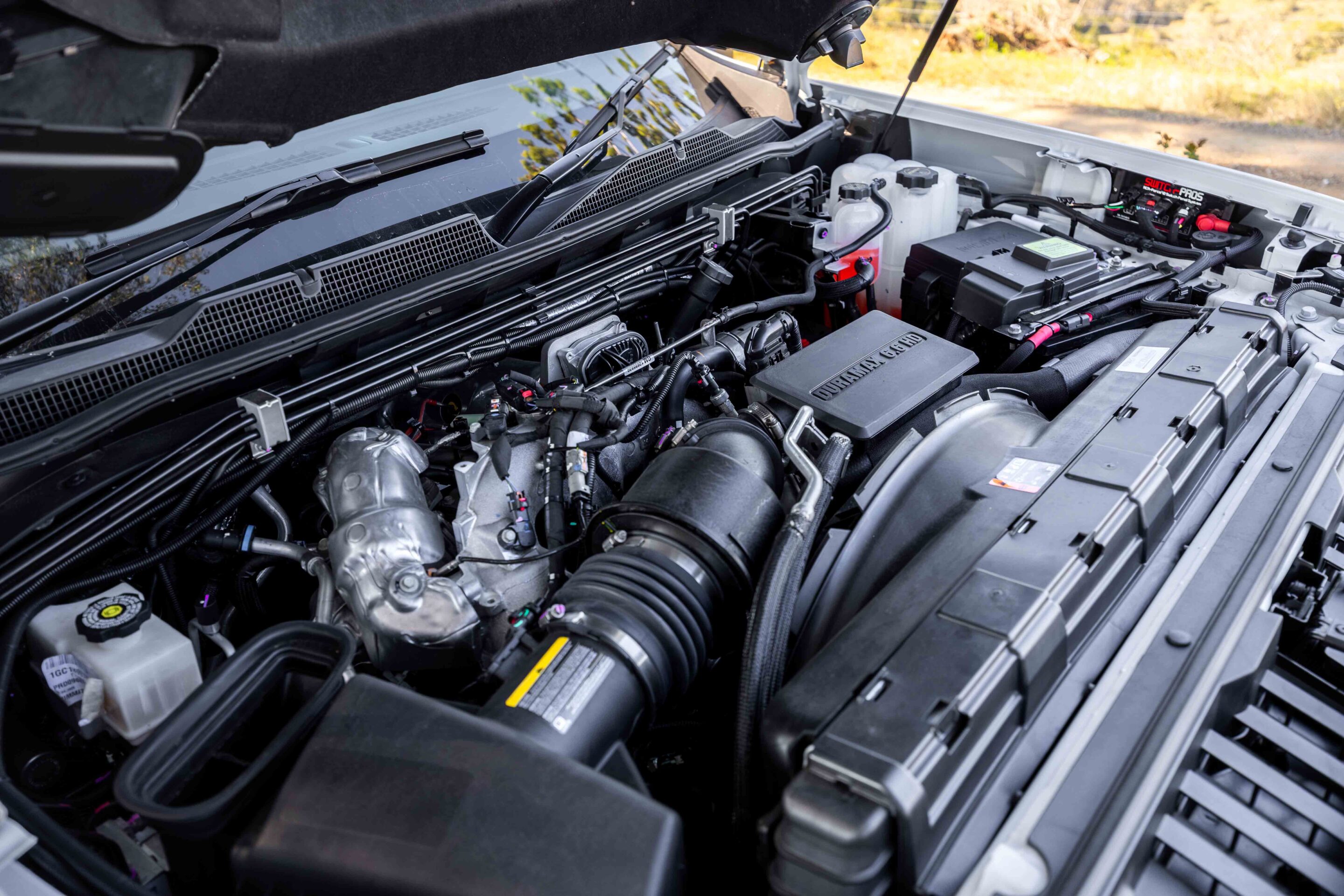Open hood engine bay of a truck showing the battery, coolant reservoir, hoses, and wiring.