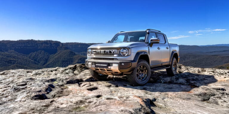 Silver Chery Stockman pickup on a rocky overlook with a blue sky and distant mountains behind it.