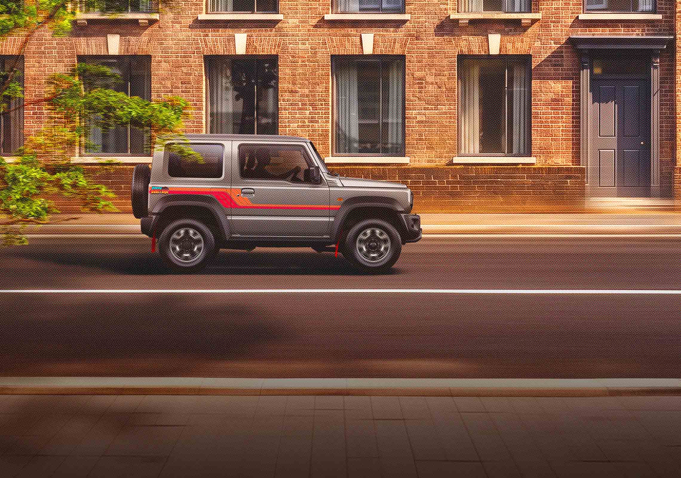 Gray SUV parked on a city street in front of a brick building with large windows and green foliage on the left.
