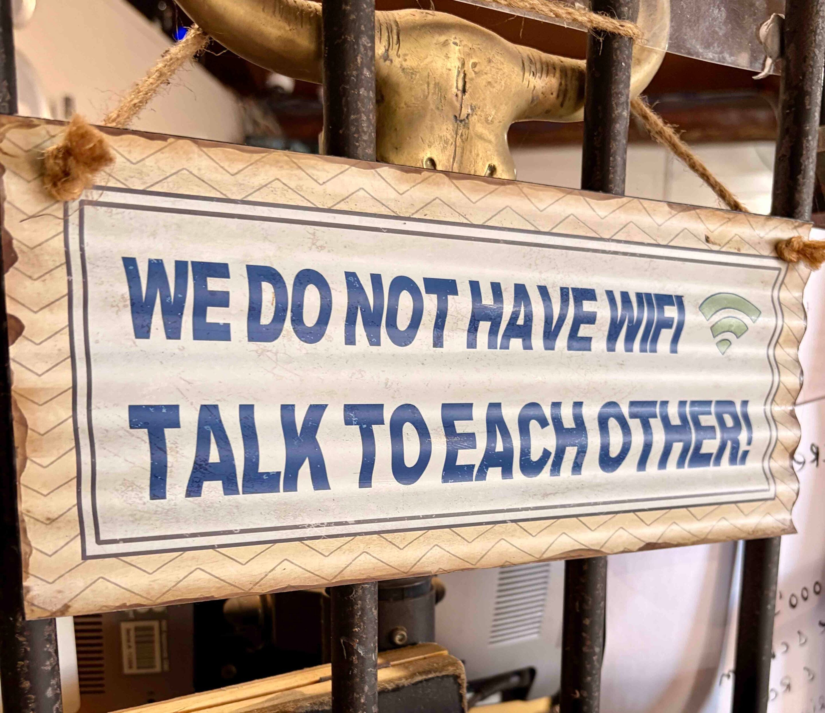 Close-up of a weathered sign with bold blue text: 'WE DO NOT HAVE' visible behind metal bars and rope, in a dusty storage area.